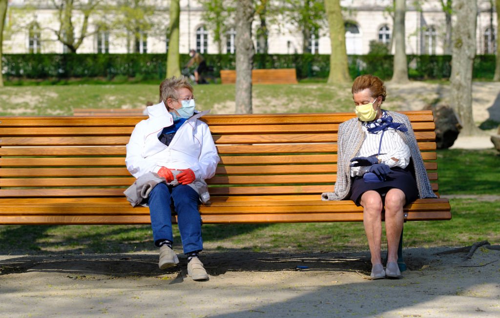 Dos mujeres con máscaras faciales se sientan al sol en el Jubelpark (Parc du Cinquantenaire - Jubilee Park) durante la pandemia de coronavirus el 6 de abril de 2020 en Bruselas, Bélgica. | Foto: Getty Images