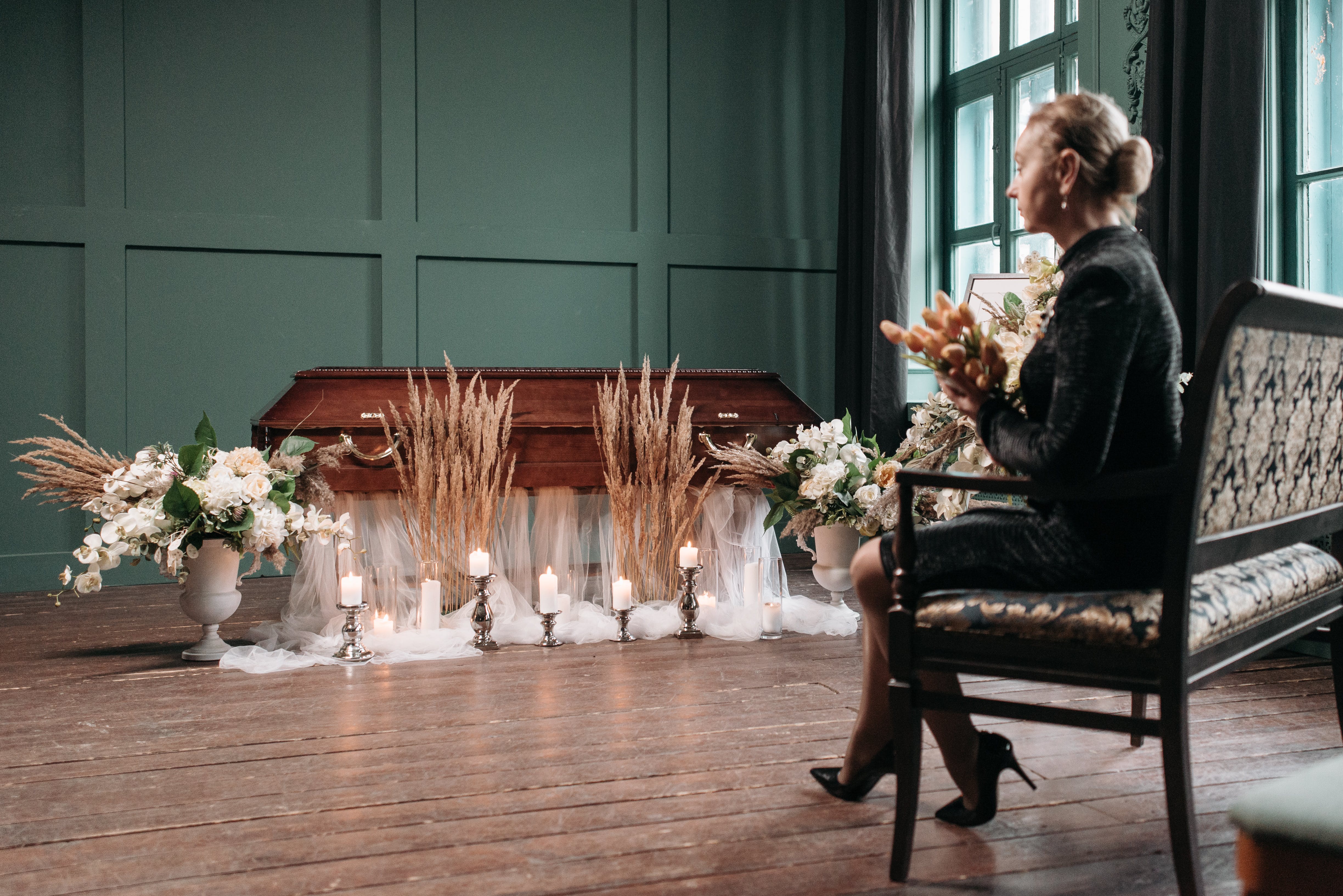 A woman sitting with flowers in hand while starring at a coffin | Source: Pexels