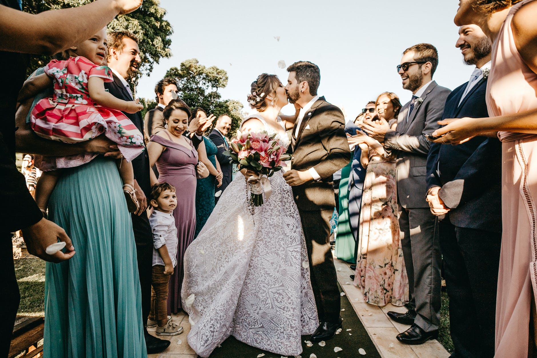 Una pareja de recién casados se da un beso mientras a su alrededor todos celebran. | Foto: Pexels