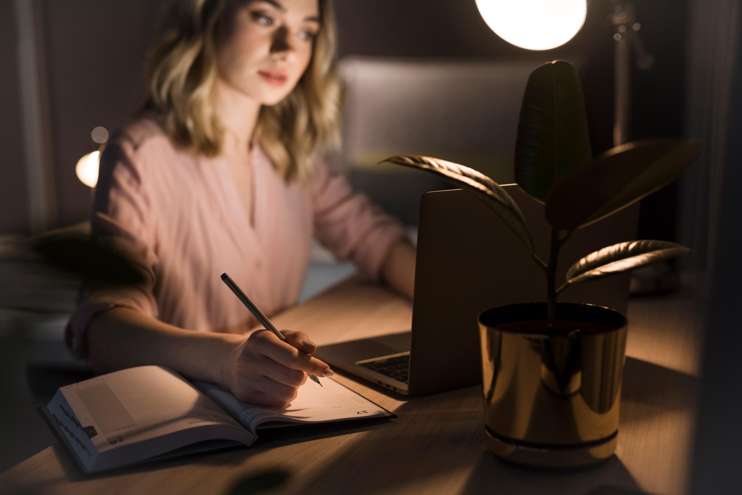 Woman seated at her desk with a pen and notebook in a room with dim lighting | Source: Shutterstock