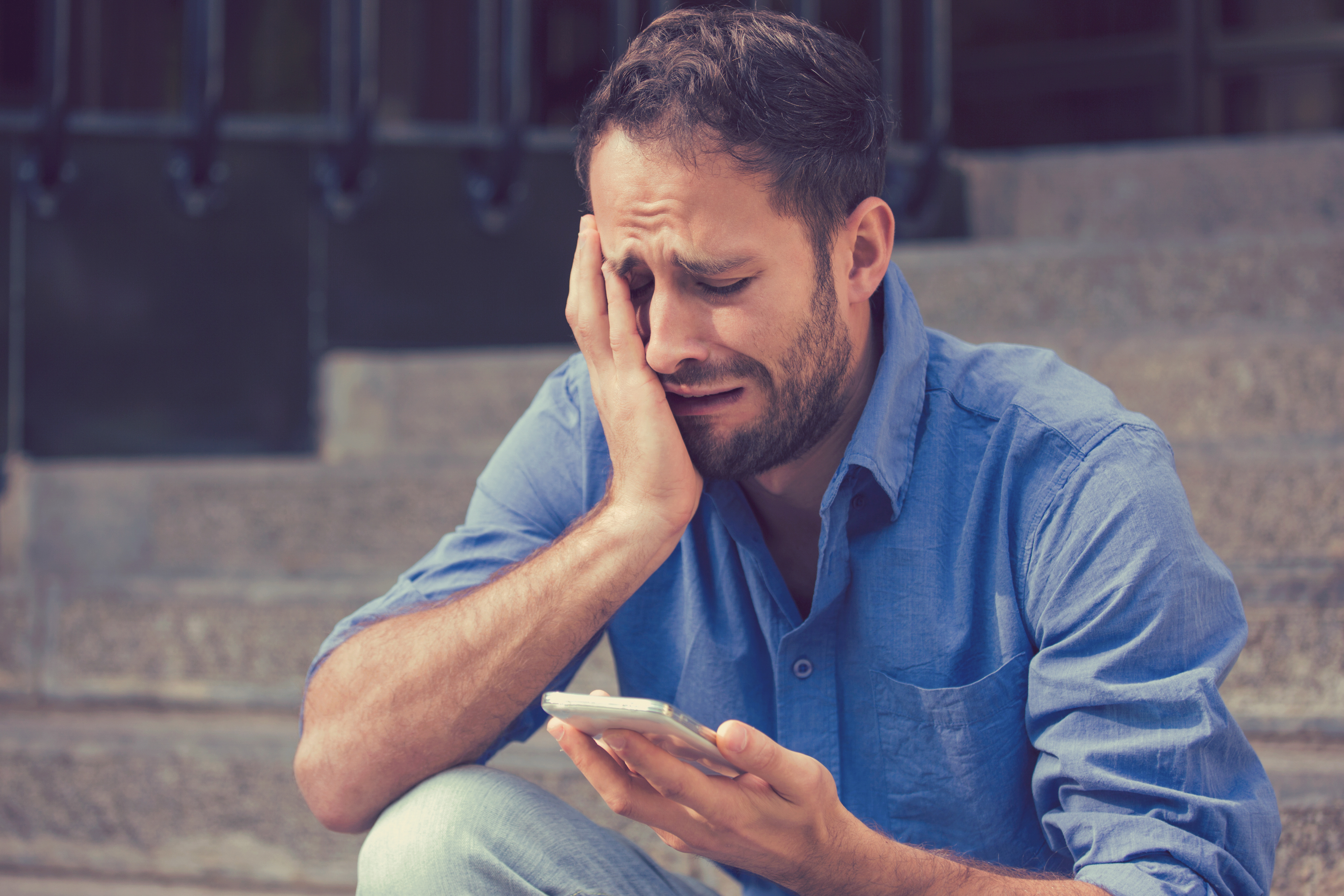 Upset man looking at his phone sitting outdoors  | Source: Shutterstock