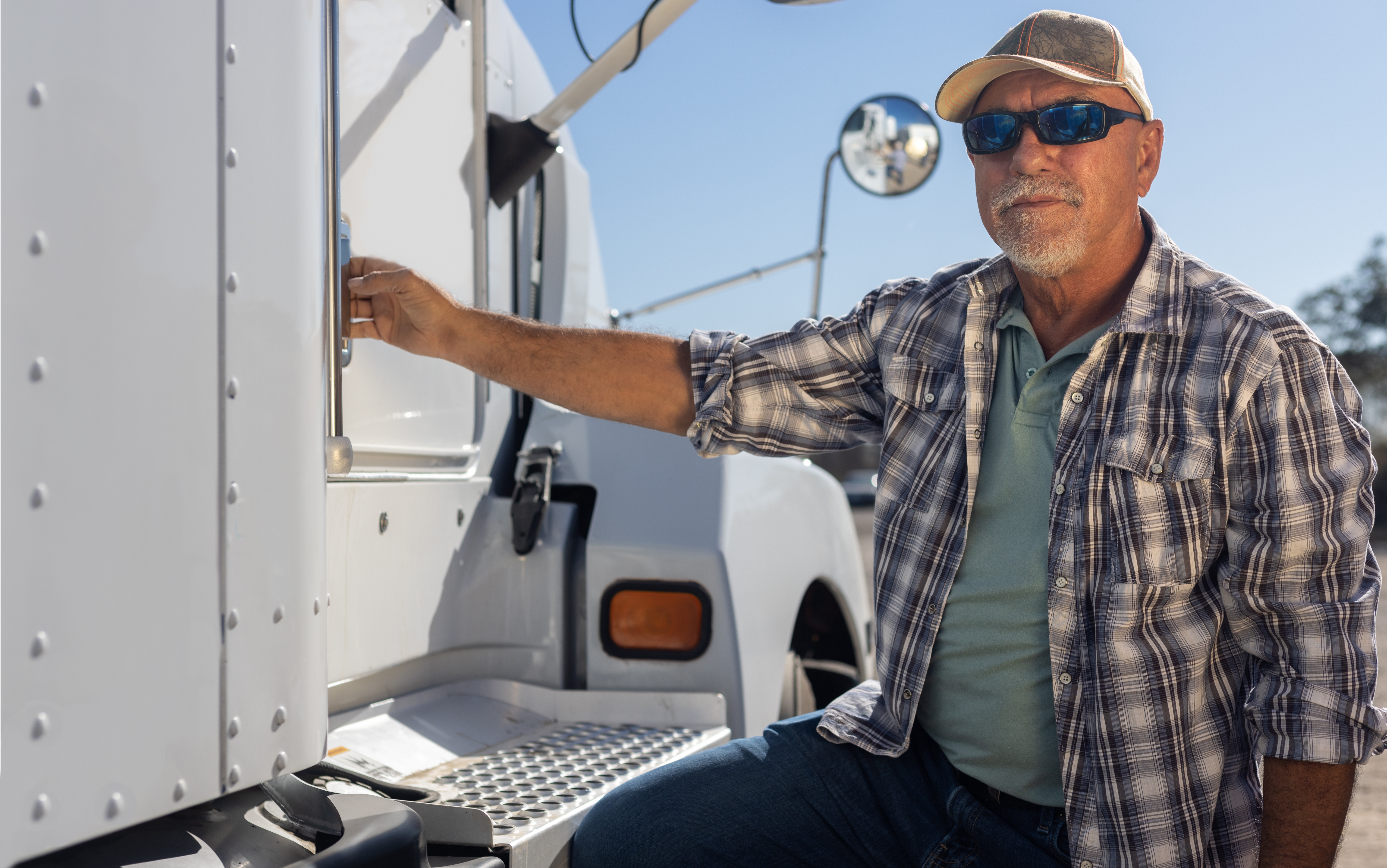 Middle aged semi truck driver sits next to truck. | Source: Shutterstock
