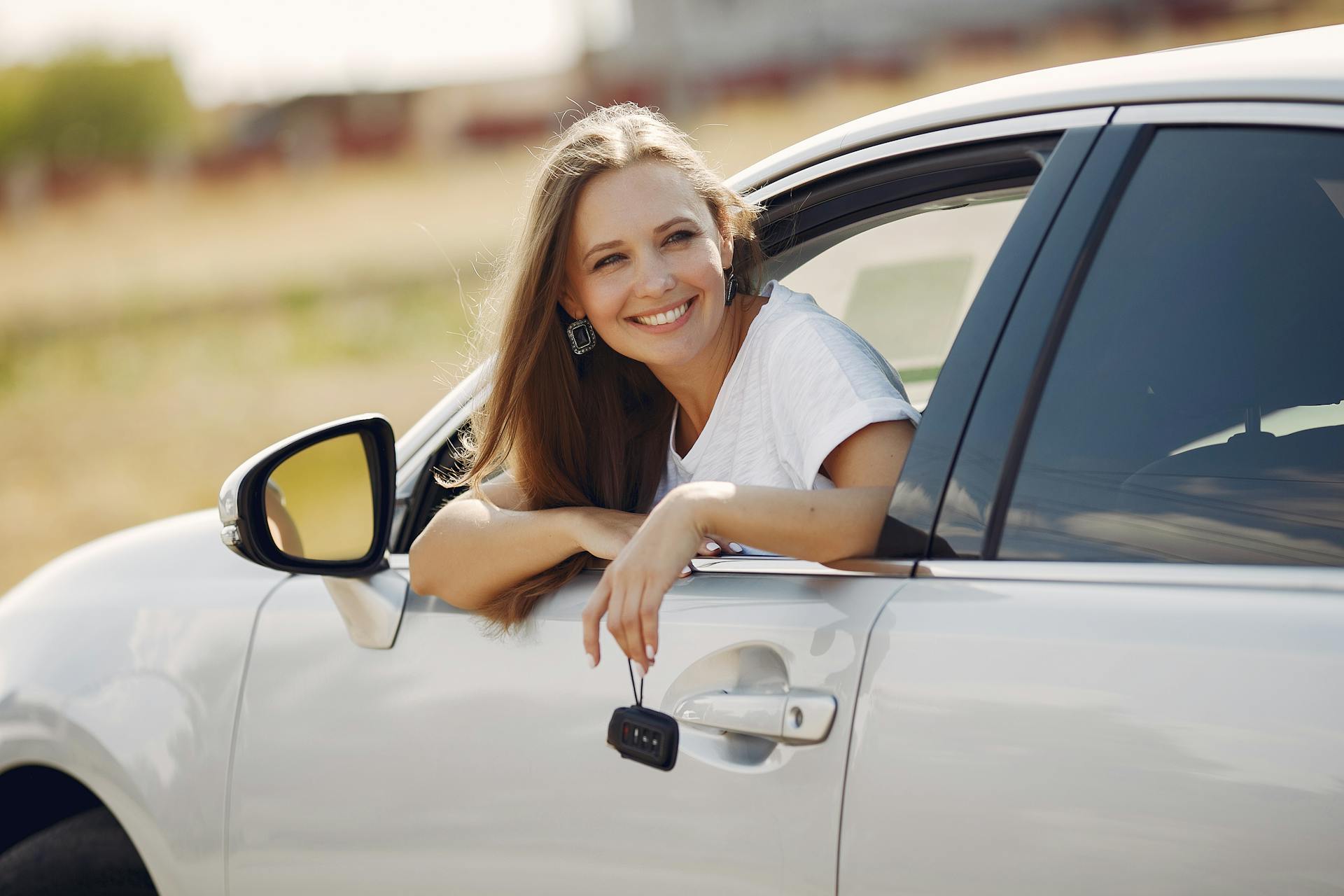 A woman peeks out from a car window while holding the keys | Source: Pexels