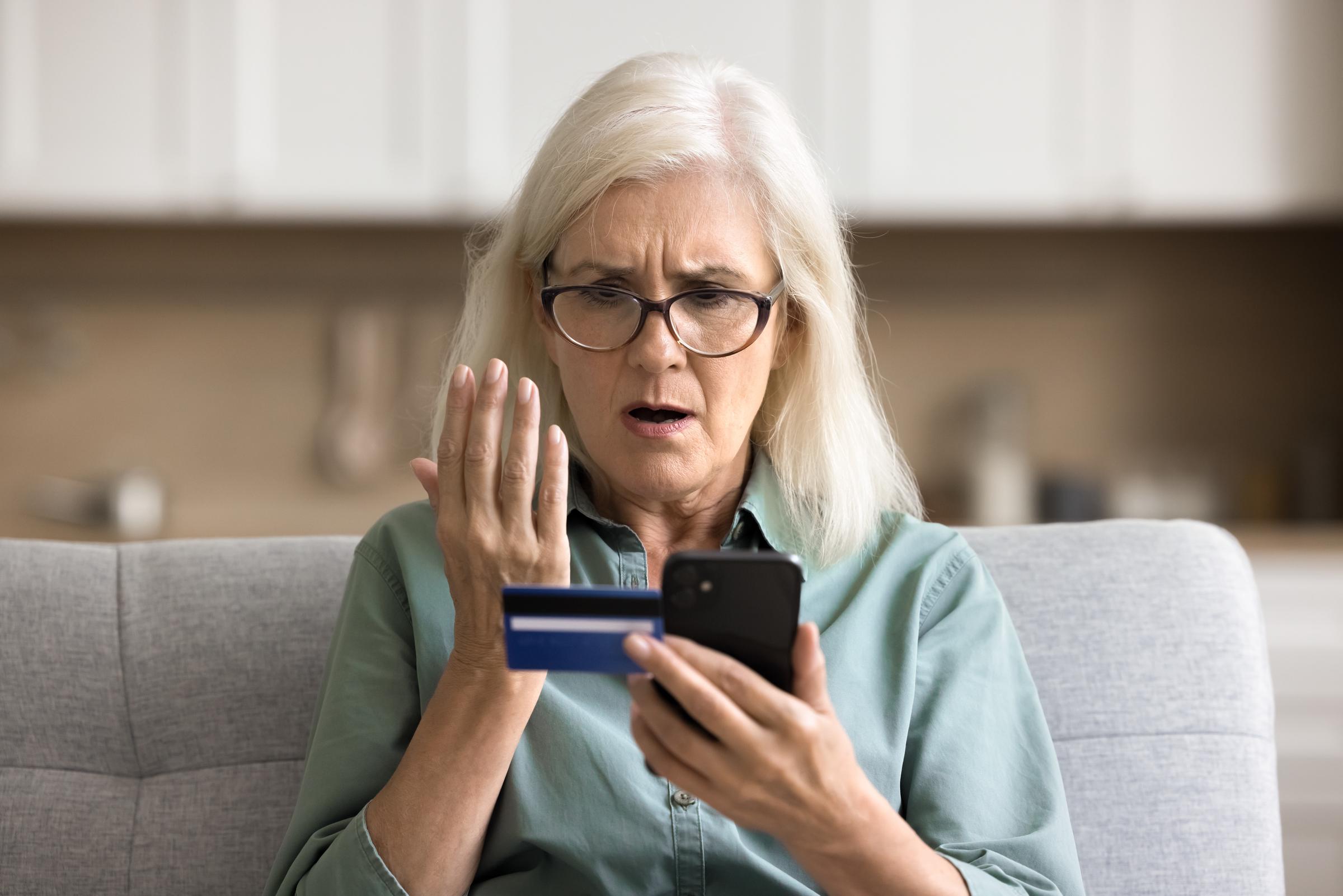 Woman appearing in disbelief as she stares at her phone and credit card | Source: Shutterstock