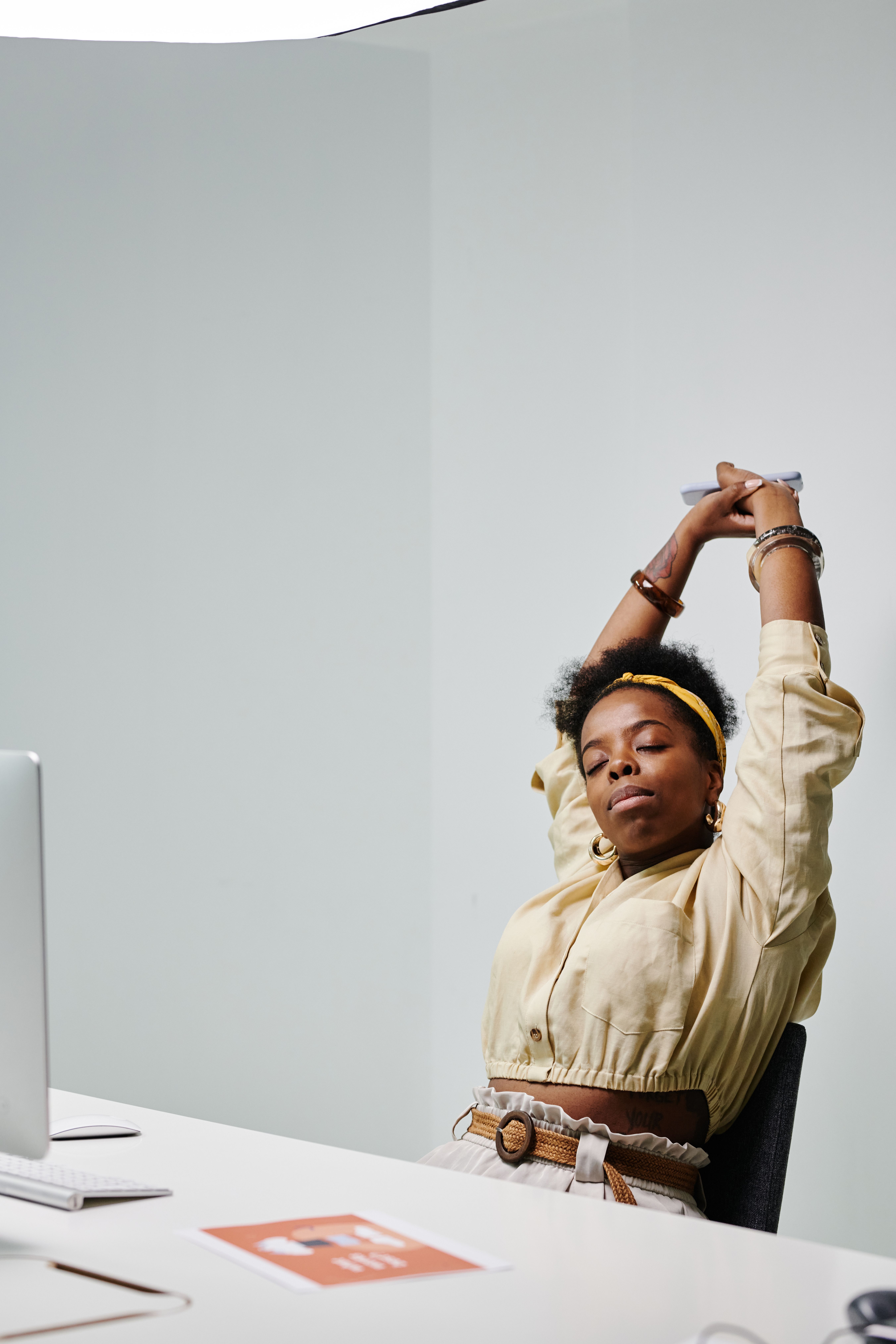 A woman stretches her arms overhead while sitting at her desk. | Source: Pexels