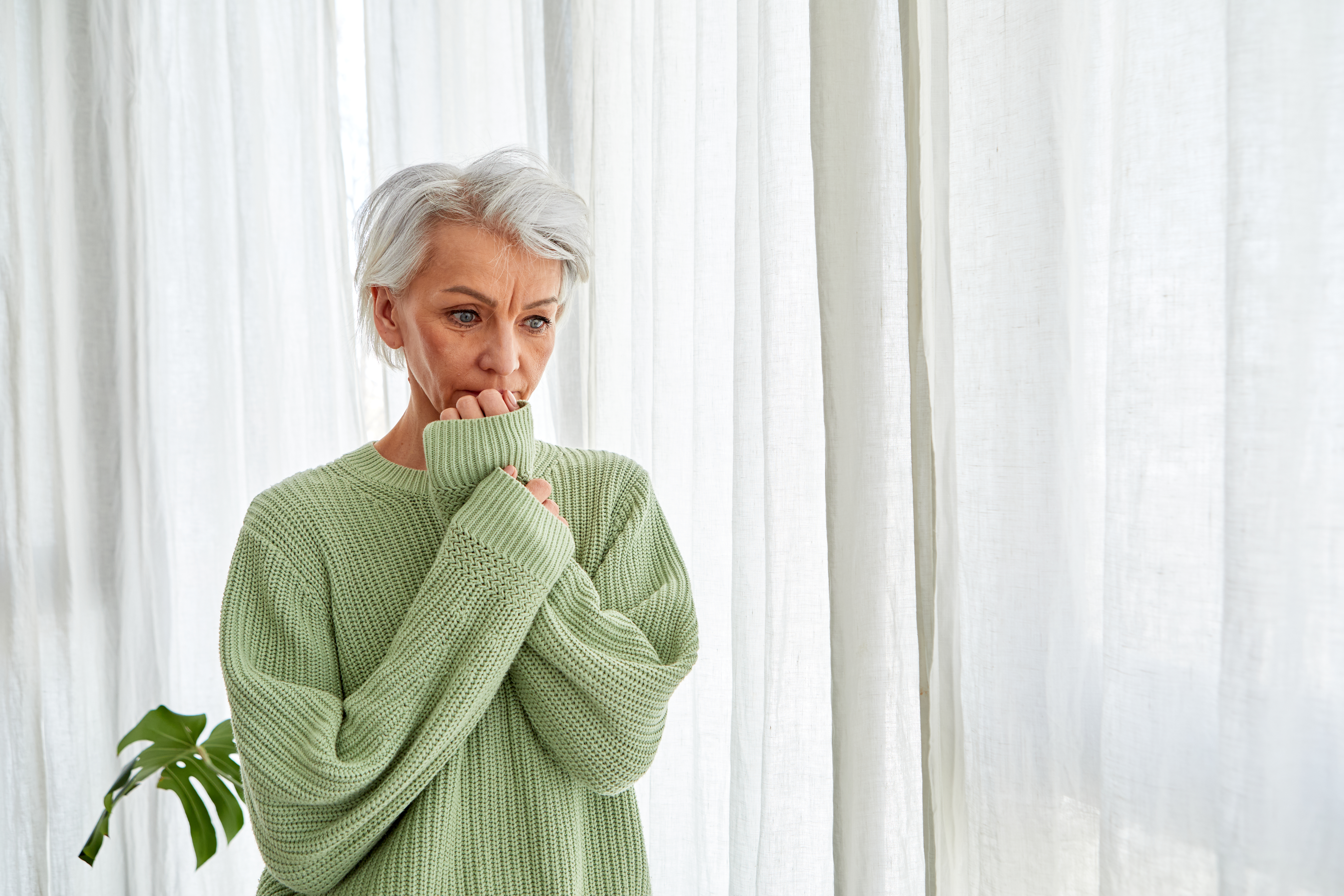 Woman with gray hair nervously bites her nails at the window | Source: Getty Images