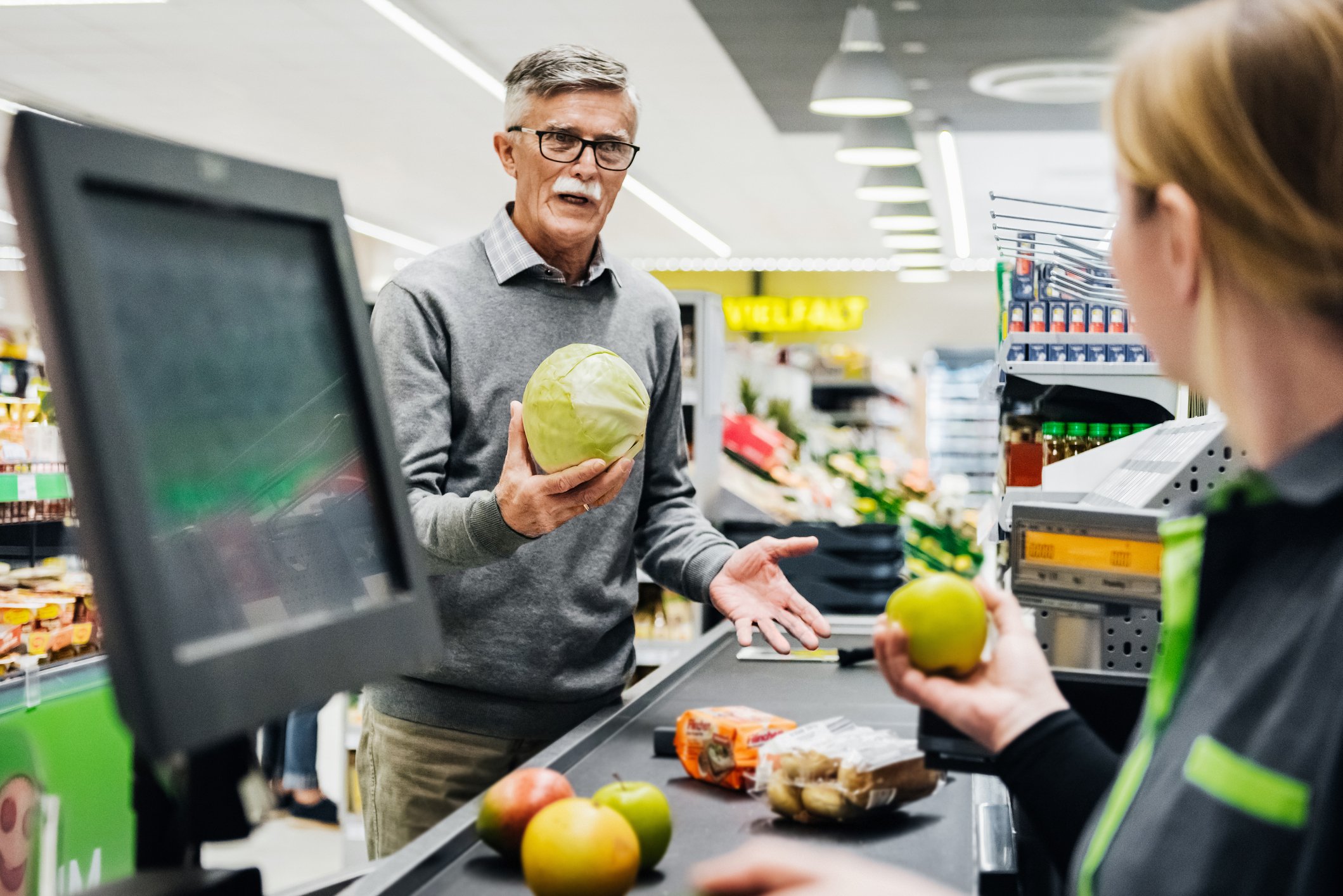 Älterer Mann, der Melone hält und mit Kassierer spricht | Quelle: Getty Images