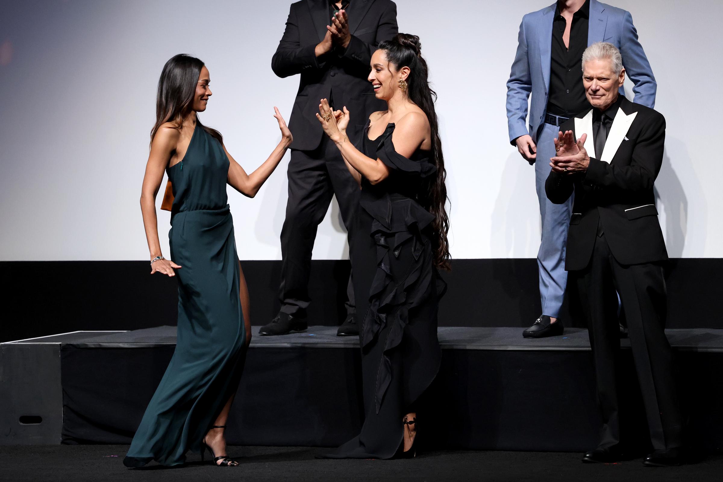 Zoe Saldaña and Oona Chaplin exchange a playful high five onstage as Stephen Lang looks on. The cast appears energized during the film's official premiere presentation.
