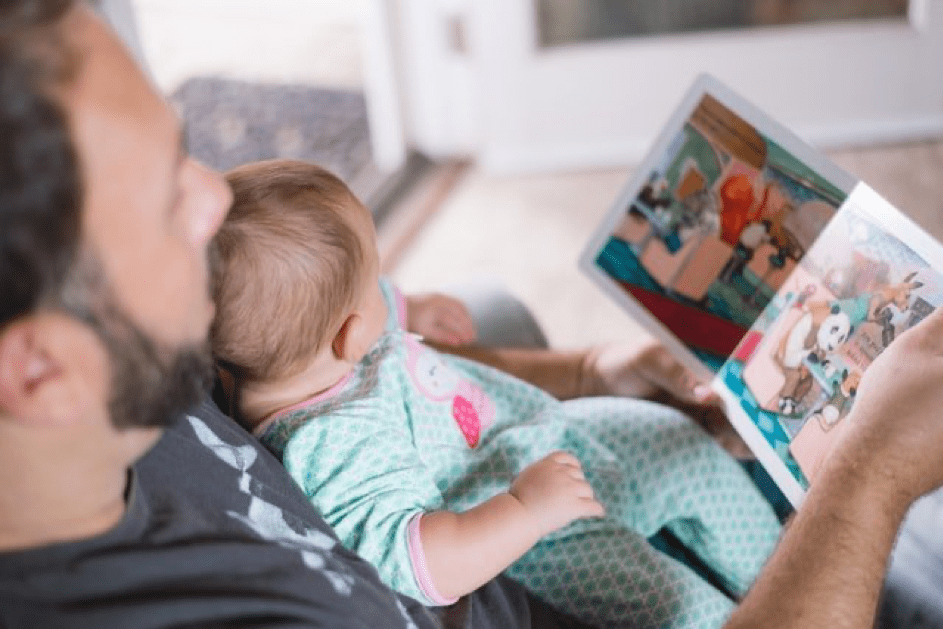 Mann hält ein Baby und liest ein Buch. | Quelle: Unsplash