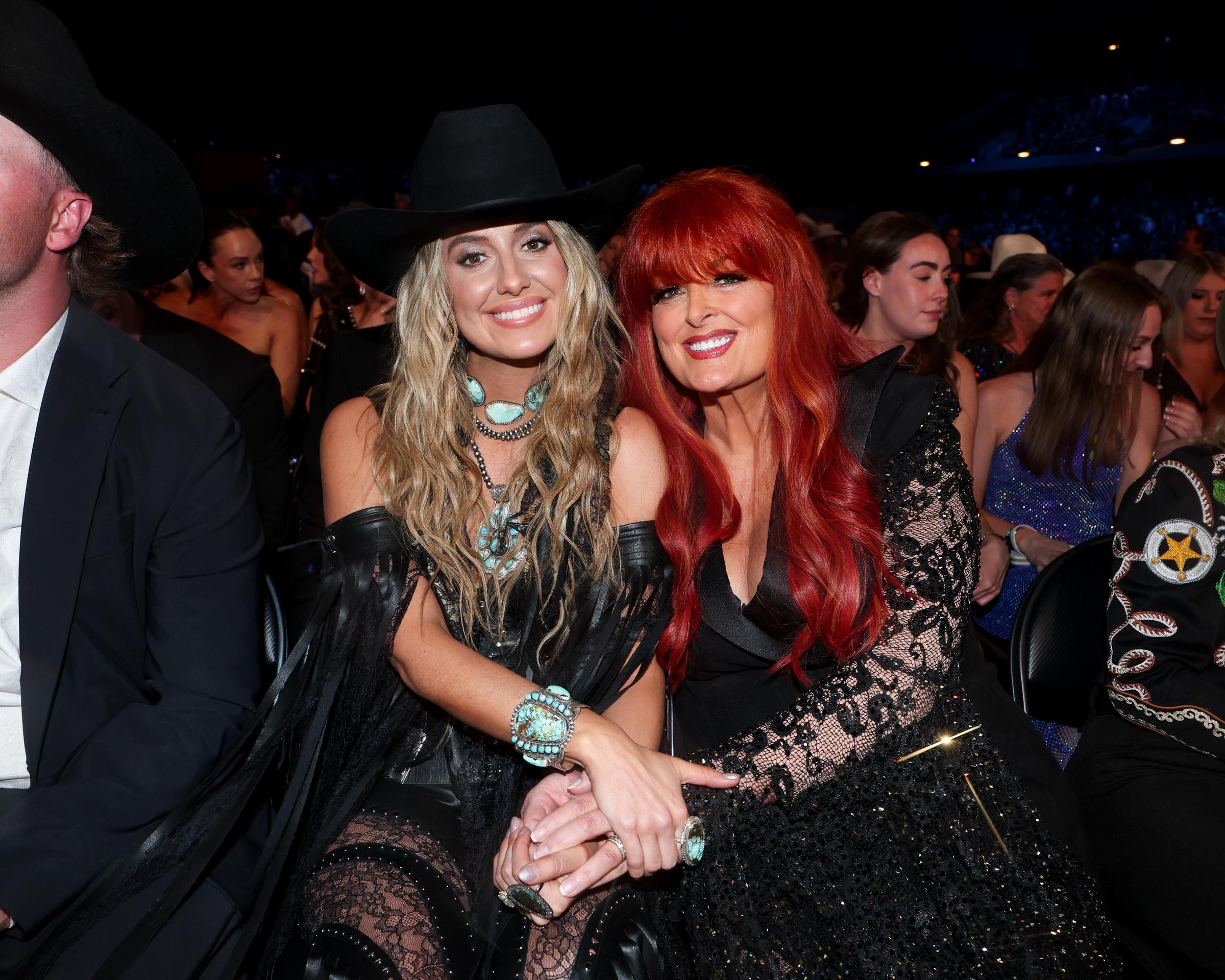 Lainey Wilson and Wynonna Judd are seen seated together at the 60th ACM Awards in Frisco, Texas. Both women appeared radiant, sharing a joyful moment and flashing big smiles while surrounded by fellow artists.