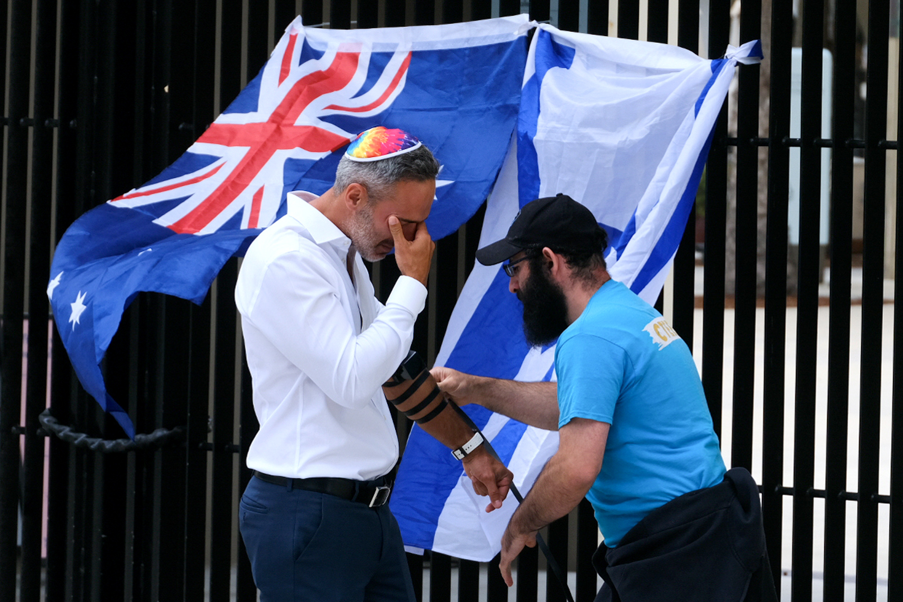 Alex Ryvchin, Co-Chief Executive Officer of the Executive Council of Australian Jewry, stood in silent prayer as another helped him wrap tefillin outside a public memorial, with Israeli and Australian flags draped nearby. The ritual, steeped in Jewish tradition, offered a moment of reflection amid the grief that gripped the community in the wake of the attack.