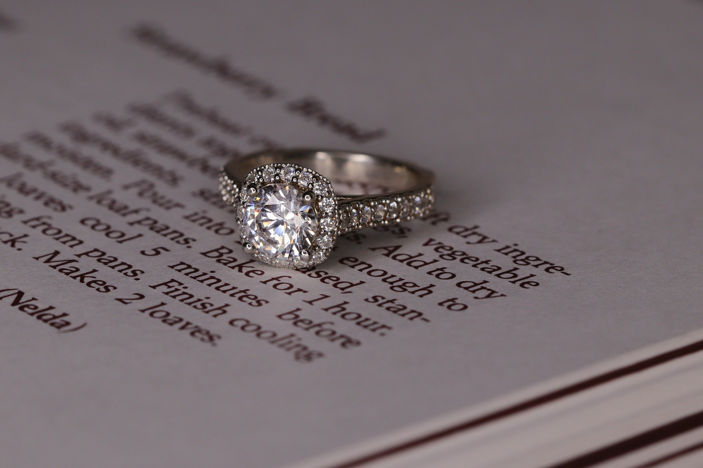 A white gold halo-style diamond engagement ring on a book | Source: Unsplash