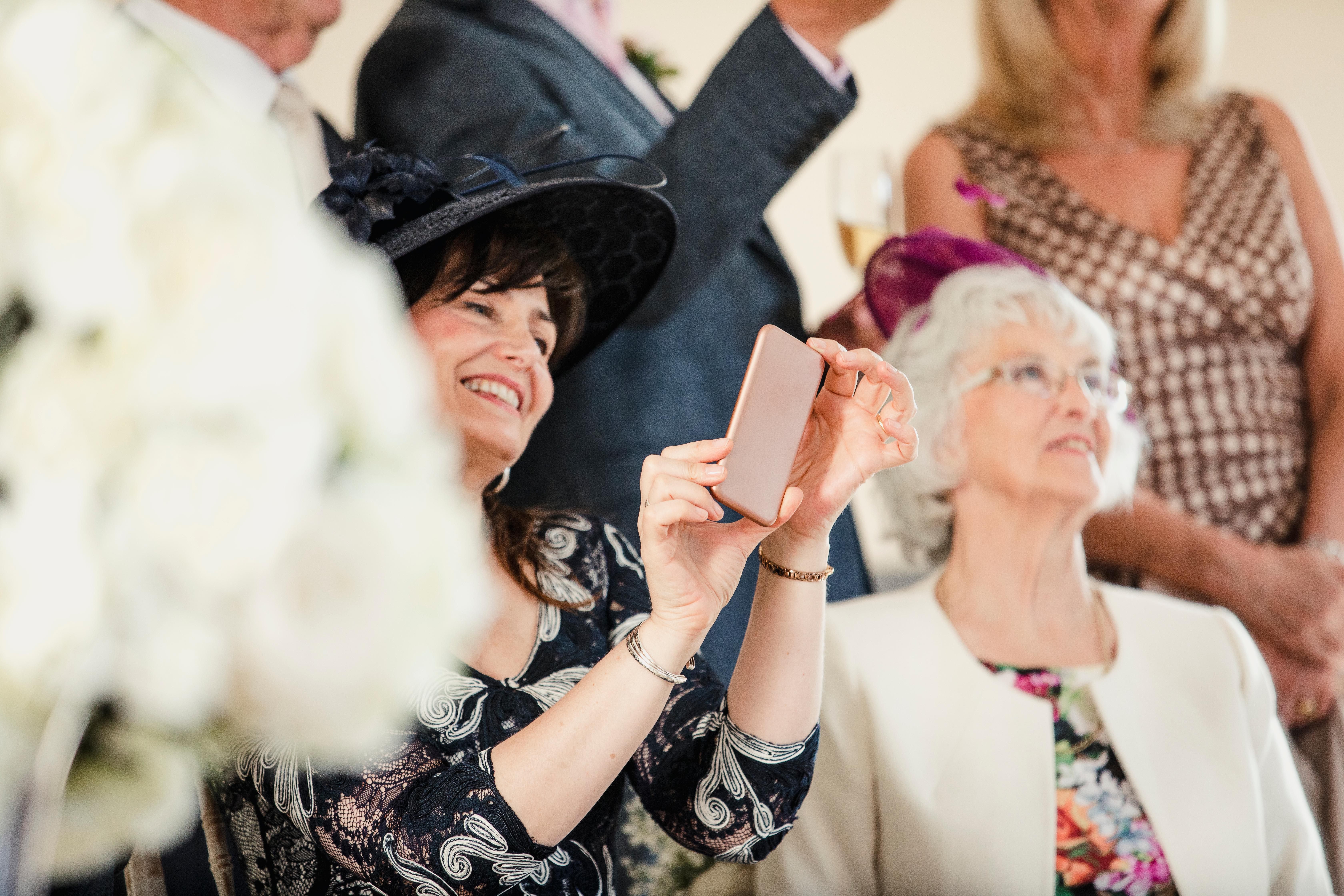 A middle-aged woman is seen holding a phone while sitting next to an older lady at a wedding ceremony | Source: Shutterstock
