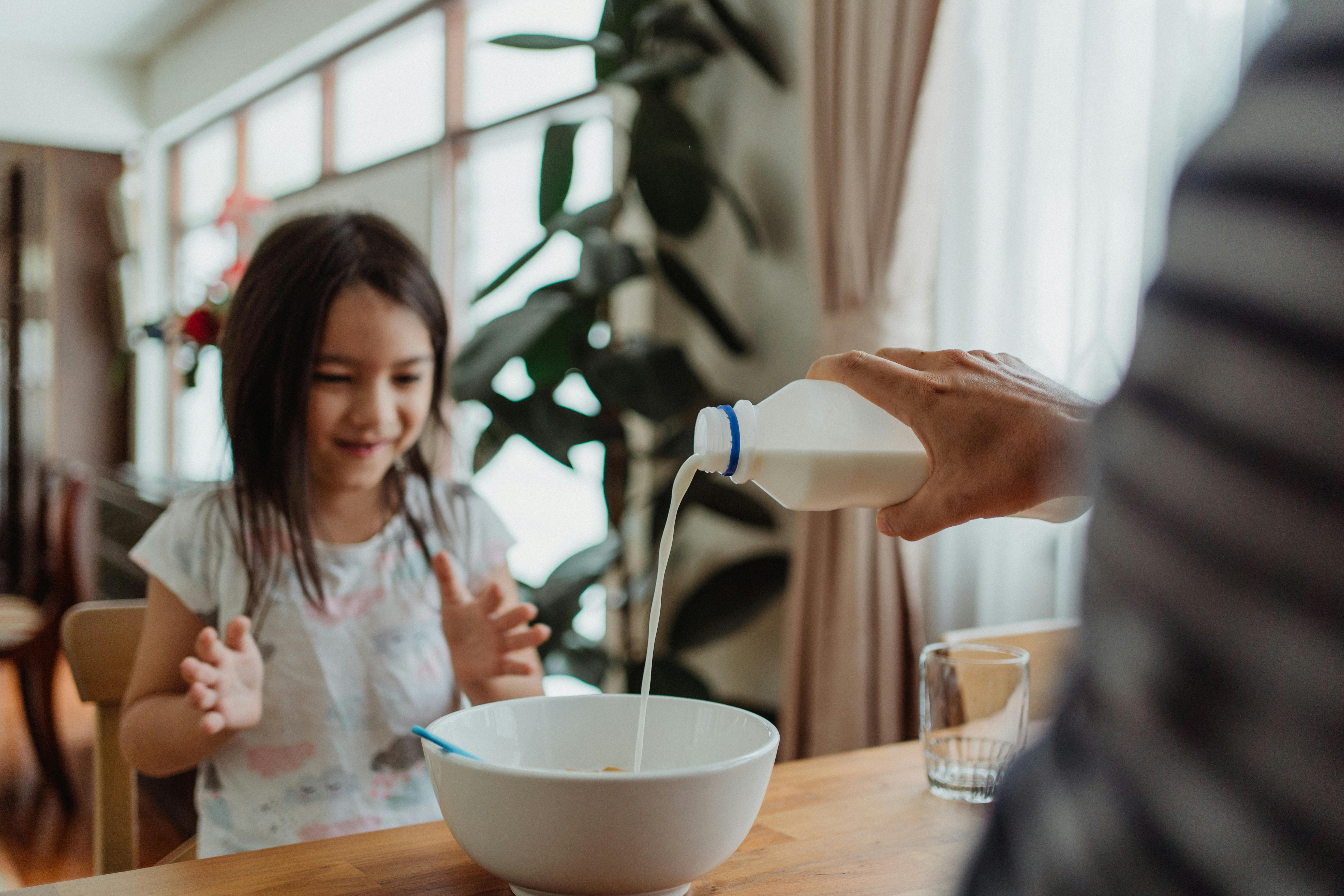 A man pouring milk into a bowl for a young girl at the breakfast table | Source: Pexels