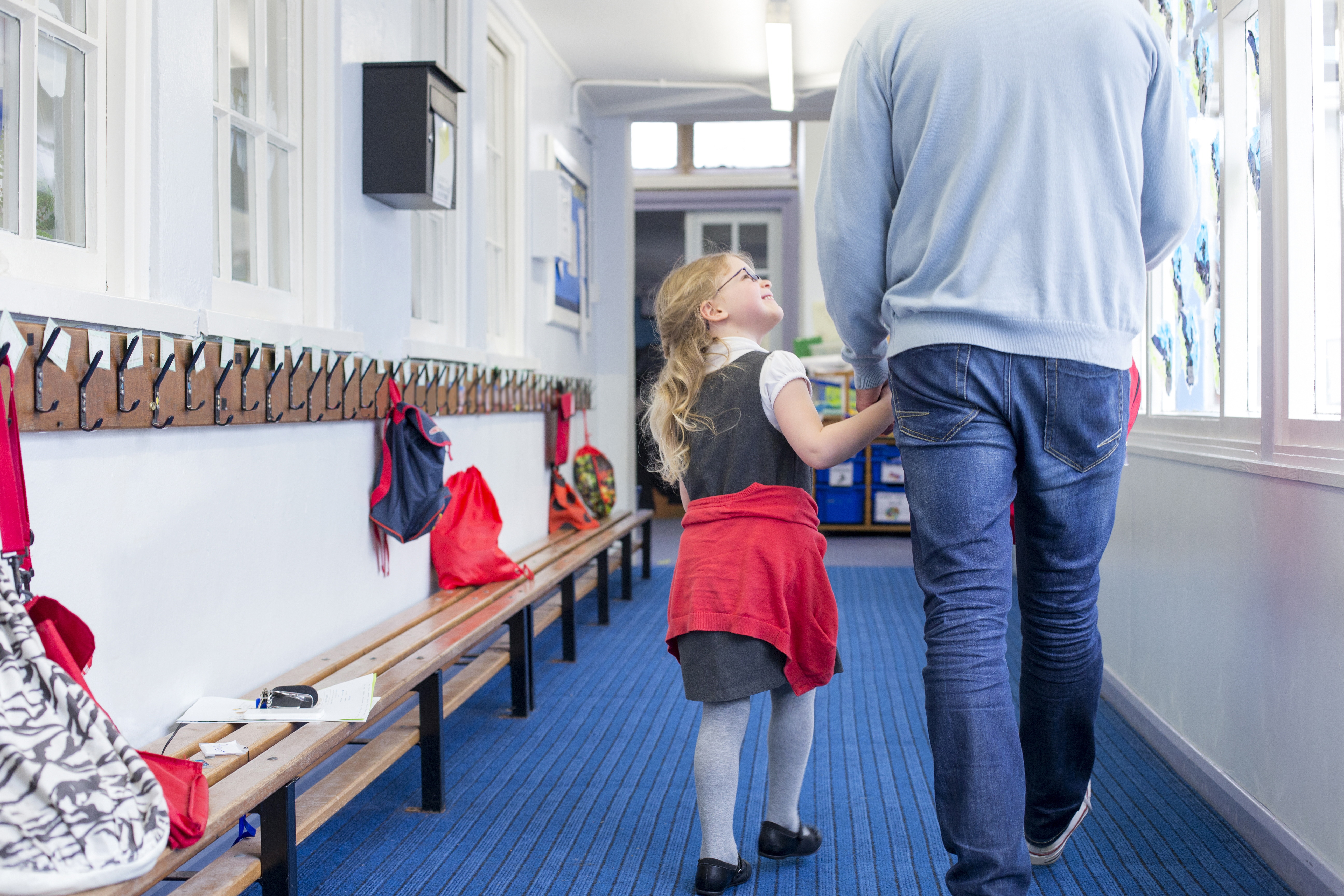 Little girl smiling and holding the hand of a man as they walk down a corridor | Source: Shutterstock