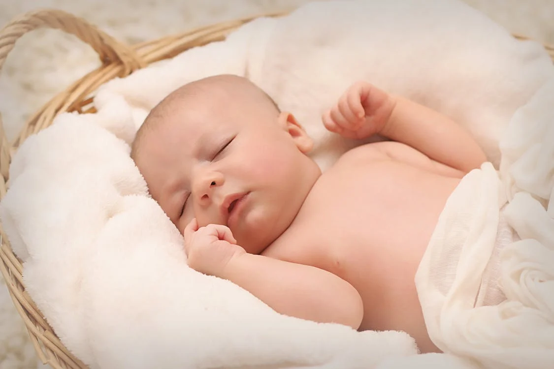Un bebé recién nacido recostado sobre mantas en una cesta de mimbre. | Foto: Pexels