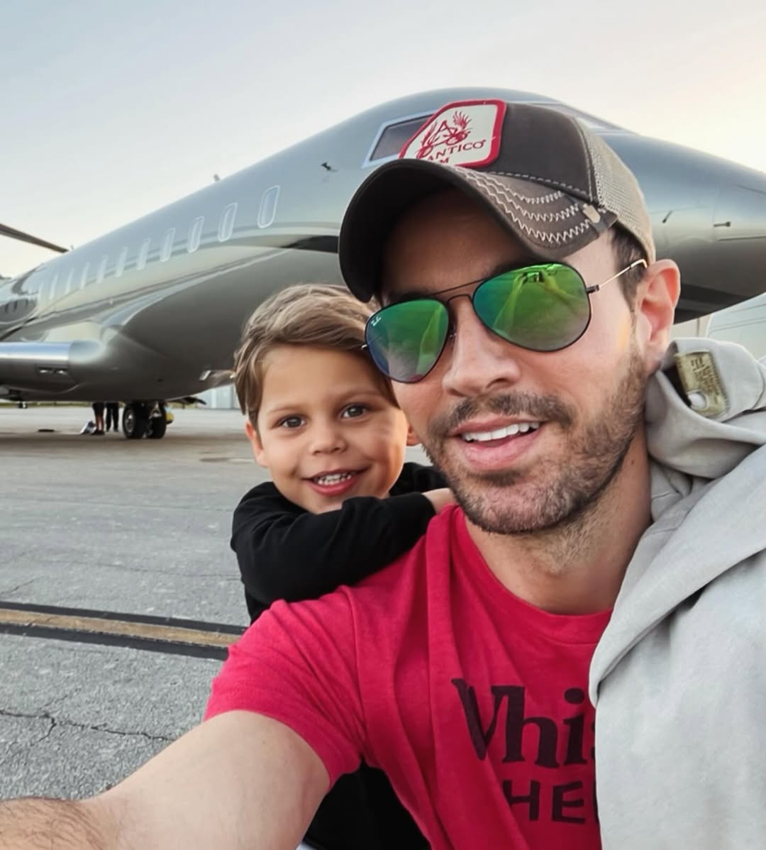Enrique and Nicholas Iglesias posing for a selfie in front of an airplane, from a post celebrating Father's Day dated June 16, 2024 | Source: Instagram/annakournikova