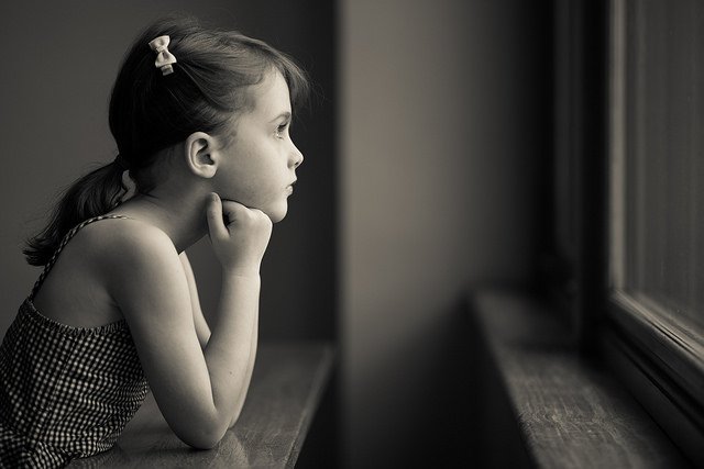 Une petite fille regardant par la fenêtre d'un air mélancolique. l Source: Flickr