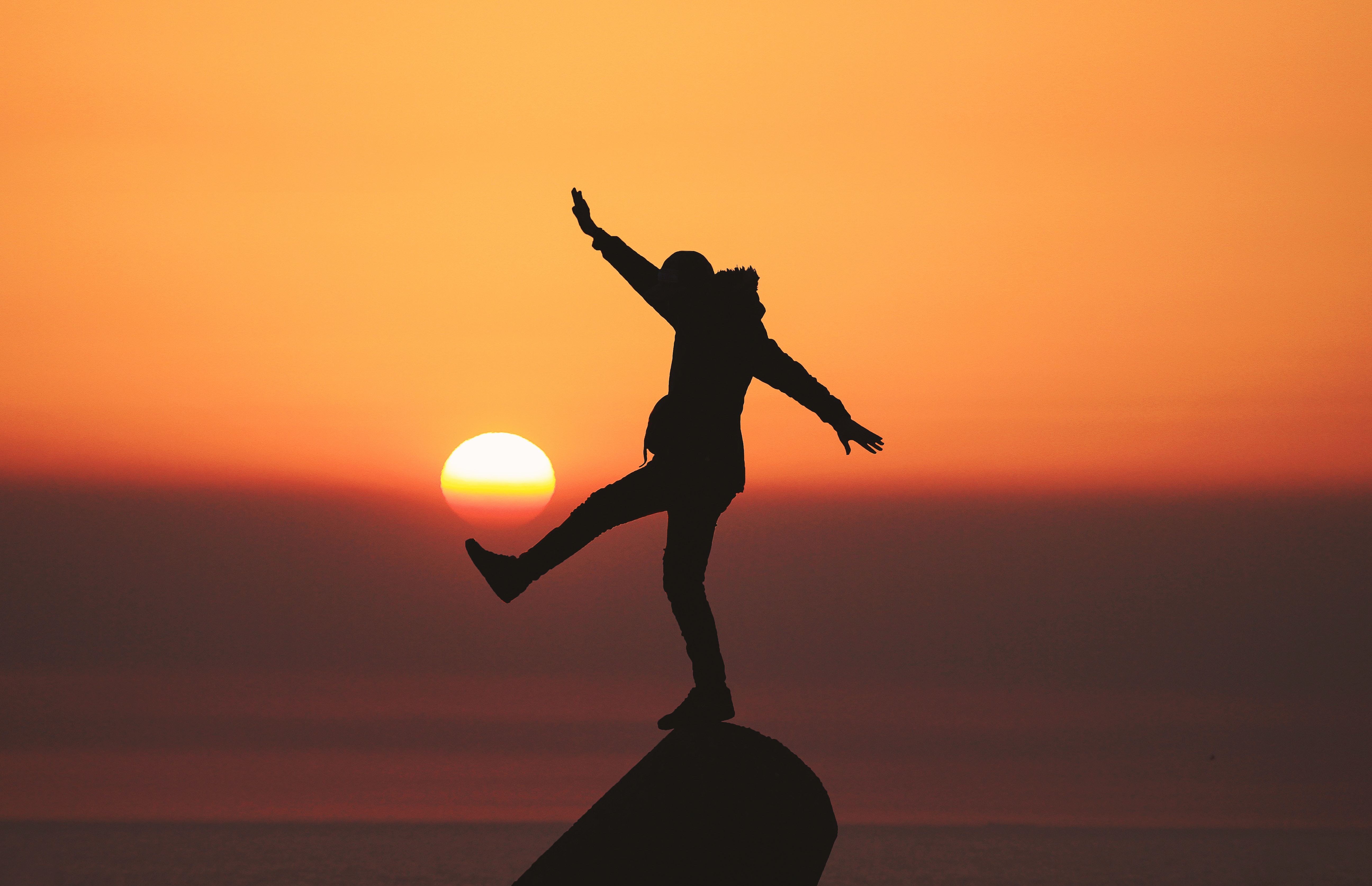 An individual balancing on a rock in front of the sunset.│Source: Unsplash