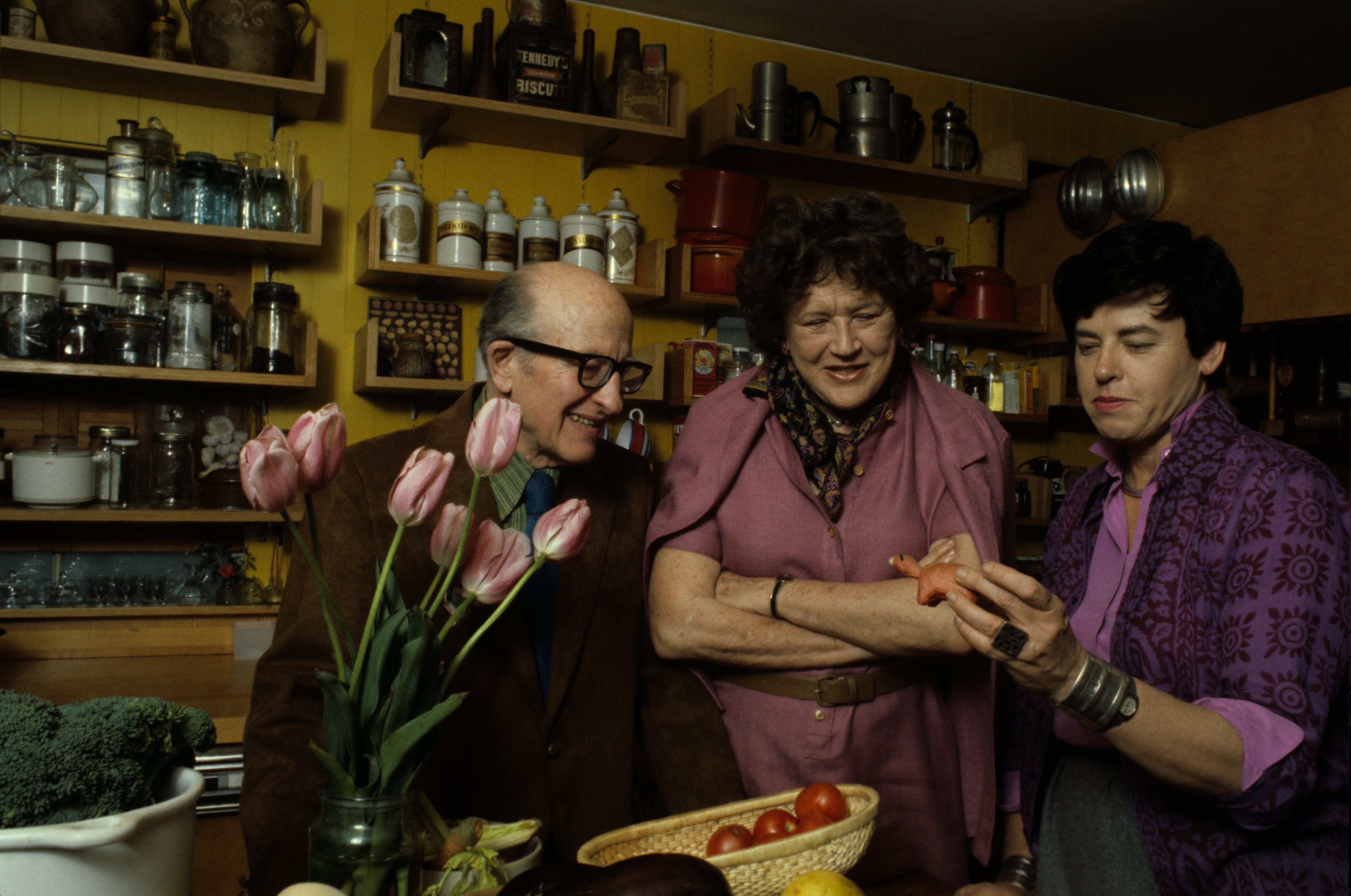 American author, and television personality Julia Child (center) and her husband, Paul Cushing Child look at a small sculpture held by an unidentified woman in a kitchen, May 1978. Photo: Getty Images