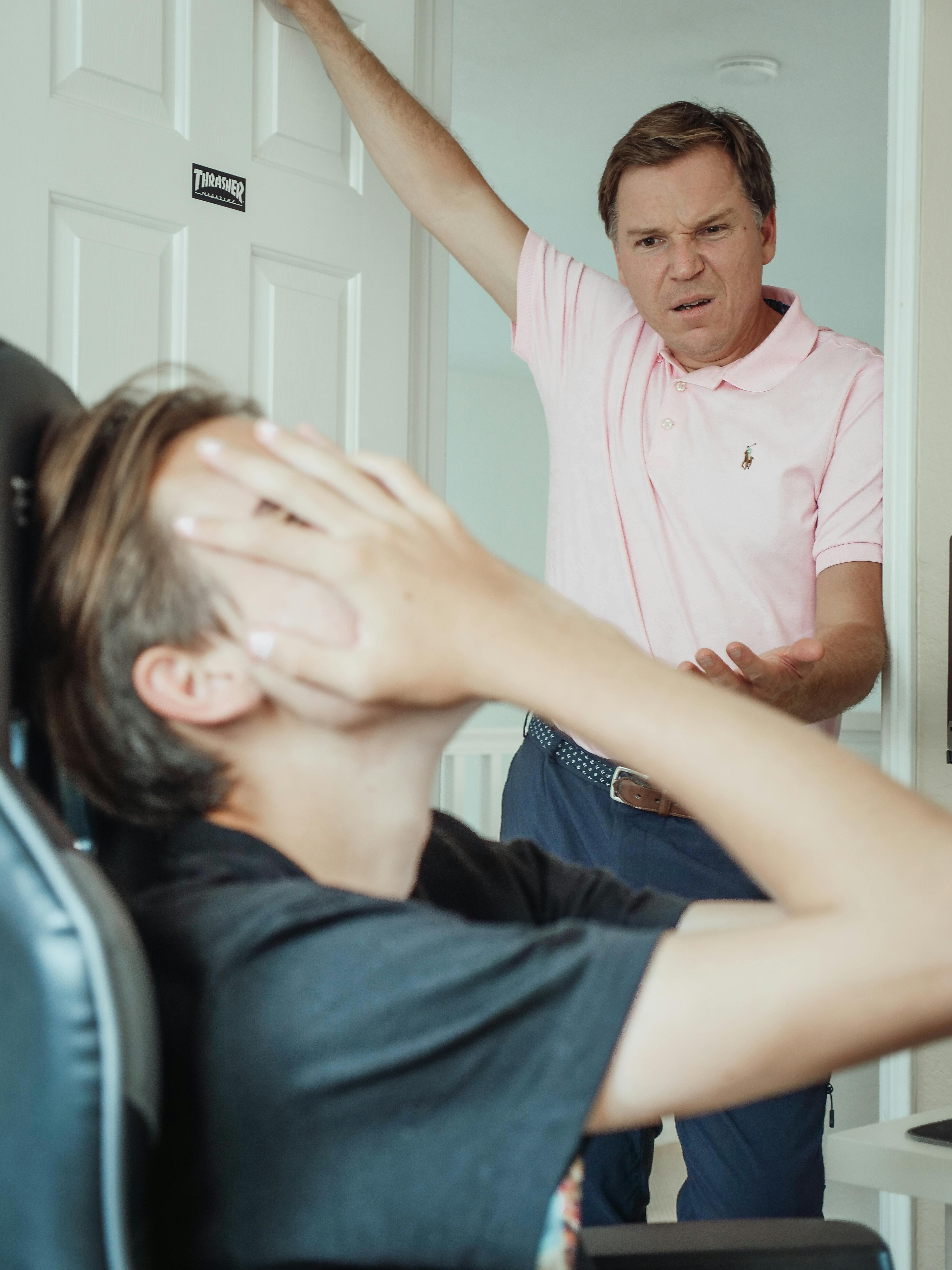 An irritated son covering his face while his father is talking to him | Source: Pexels