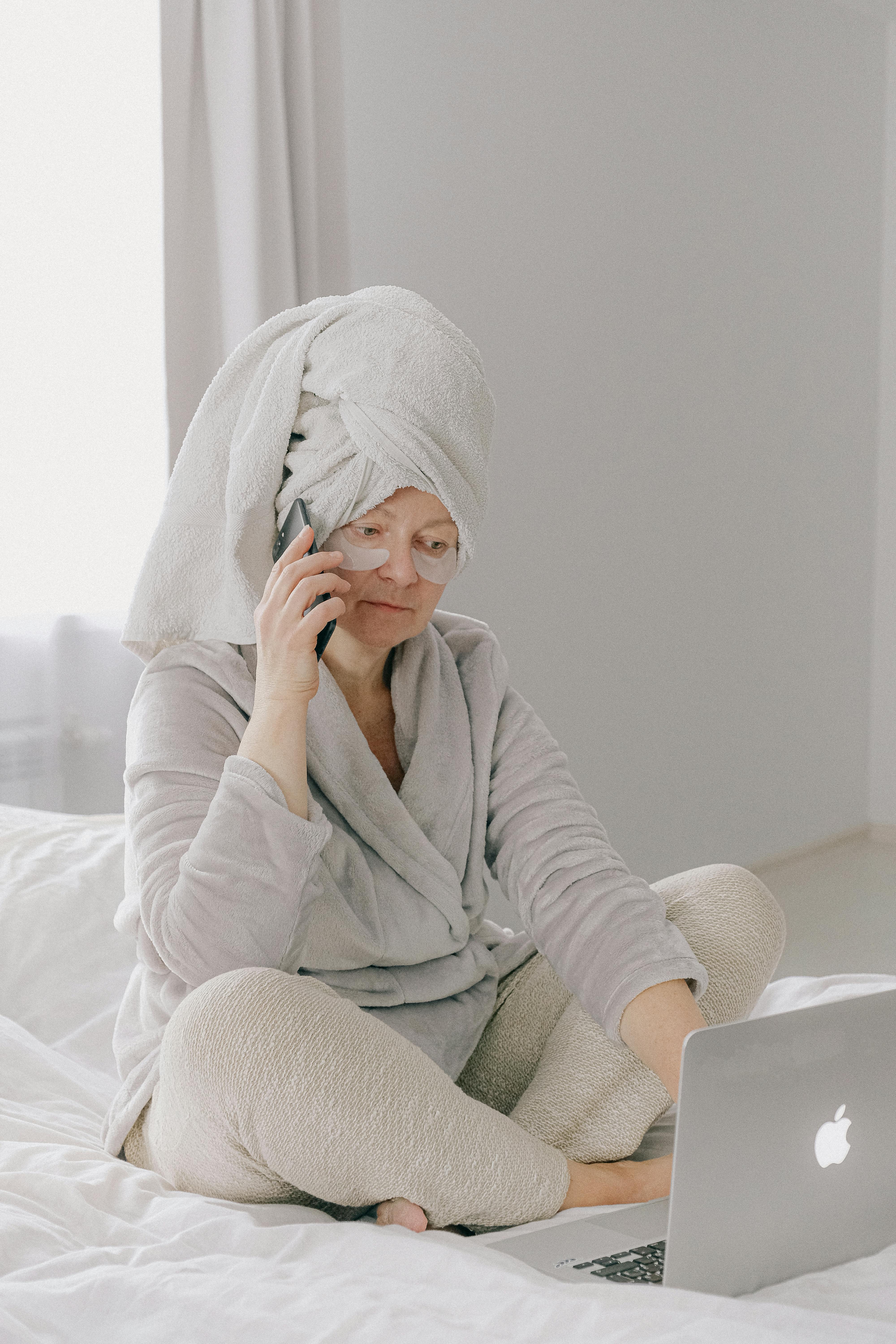 A woman in her gown and pajamas on the phone and laptop | Source: Pexels