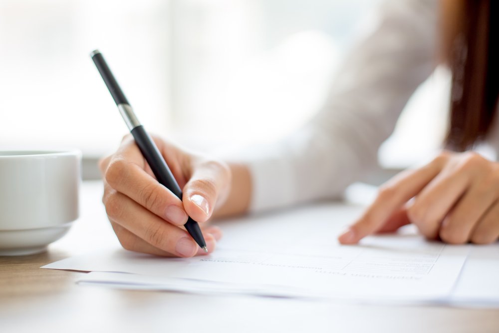 Hand of businesswoman writing on paper in office. | Photo: Shutterstock