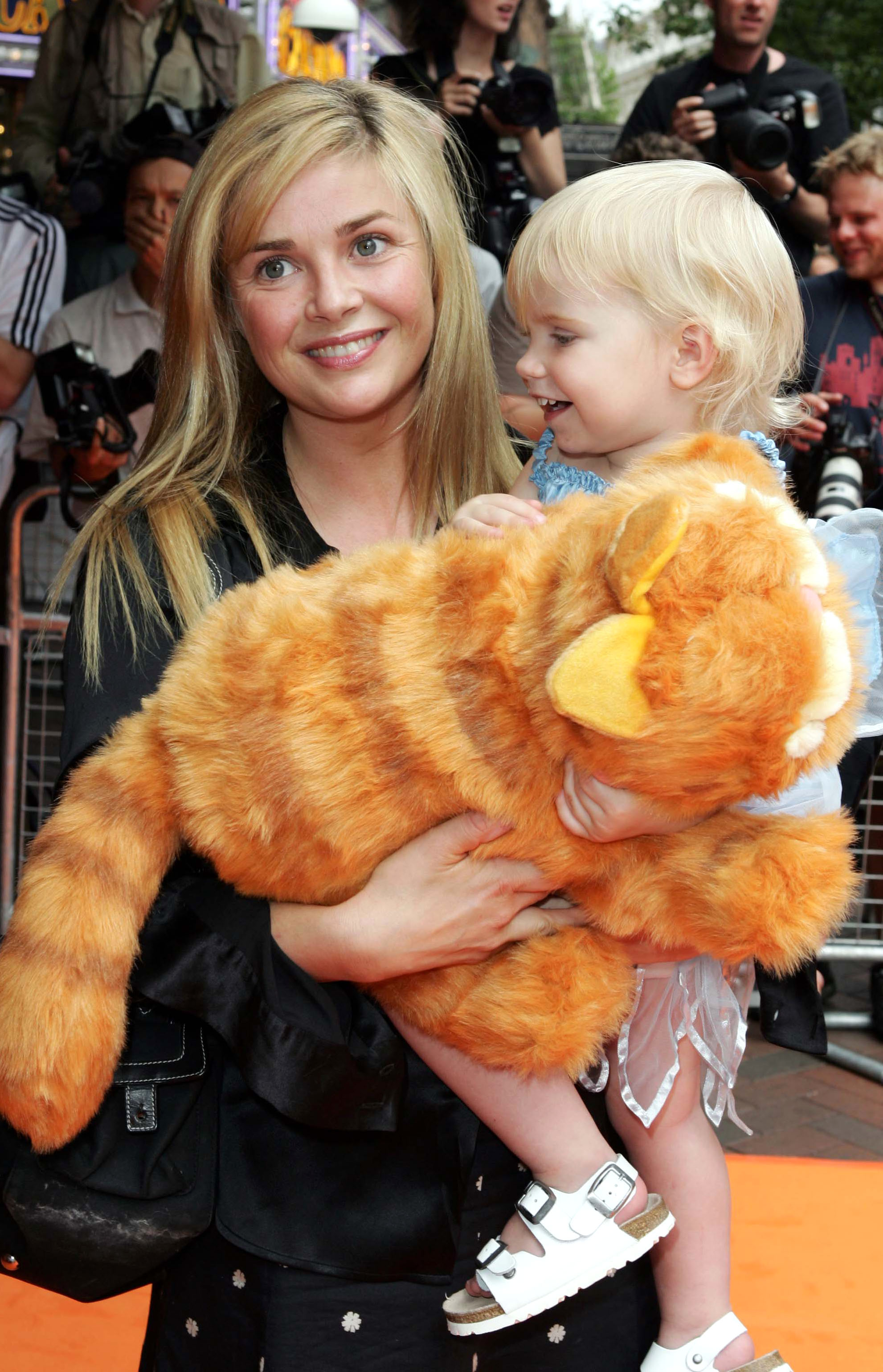 Porter holds her small daughter Honey on her hip, both clutching a large plush Garfield toy between them. Honey, in a pale blue top and tutu skirt, turns to look at her mother with a wide grin as Porter beams at the cameras. Pictured at the "Garfield" premiere in London's West End, July 2004.