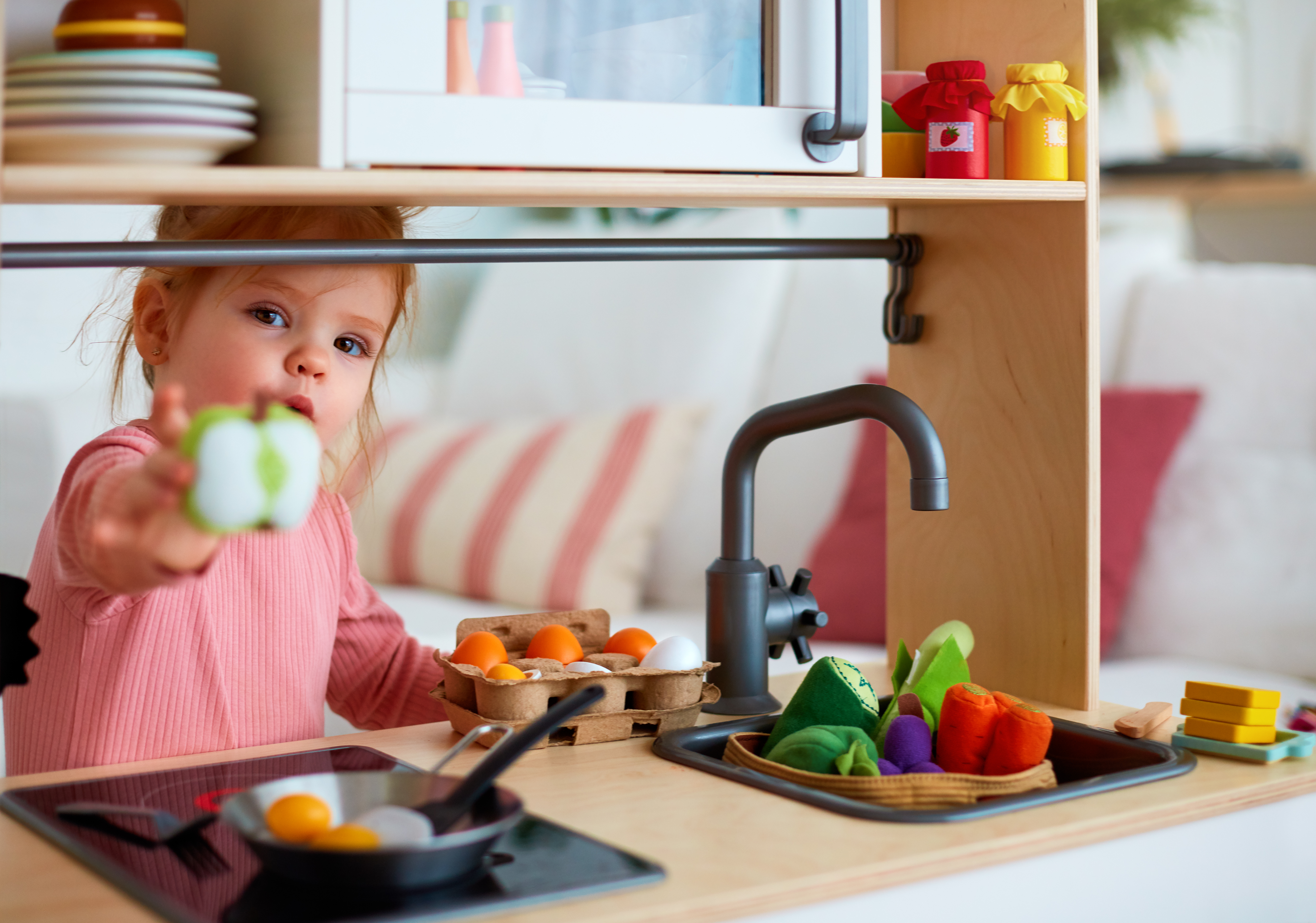 A child holding out a plastic apple in a toy kitchen | Source: Shutterstock