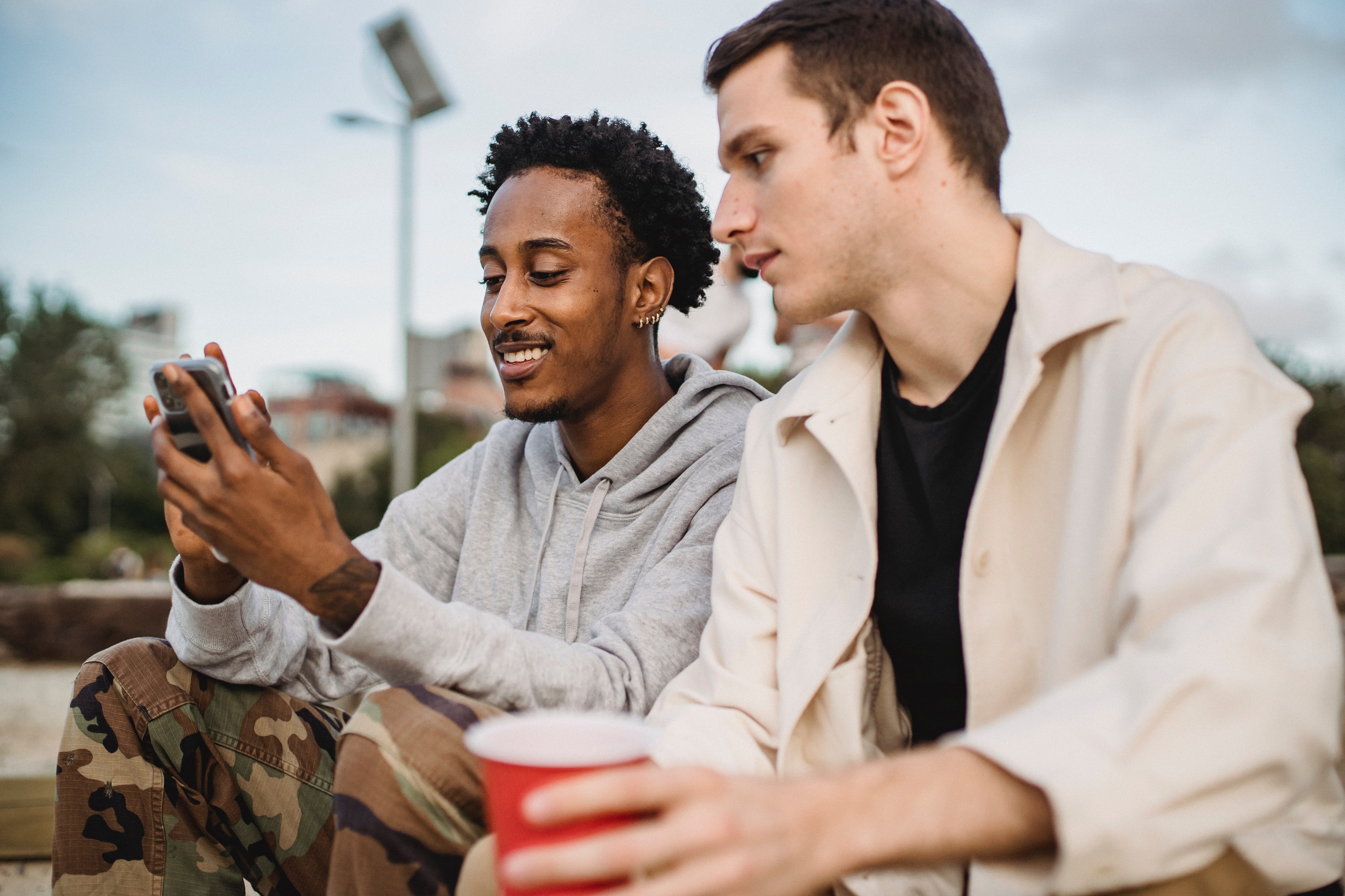 Cheerful man showing his phone to a friend  | Photo: Pexels