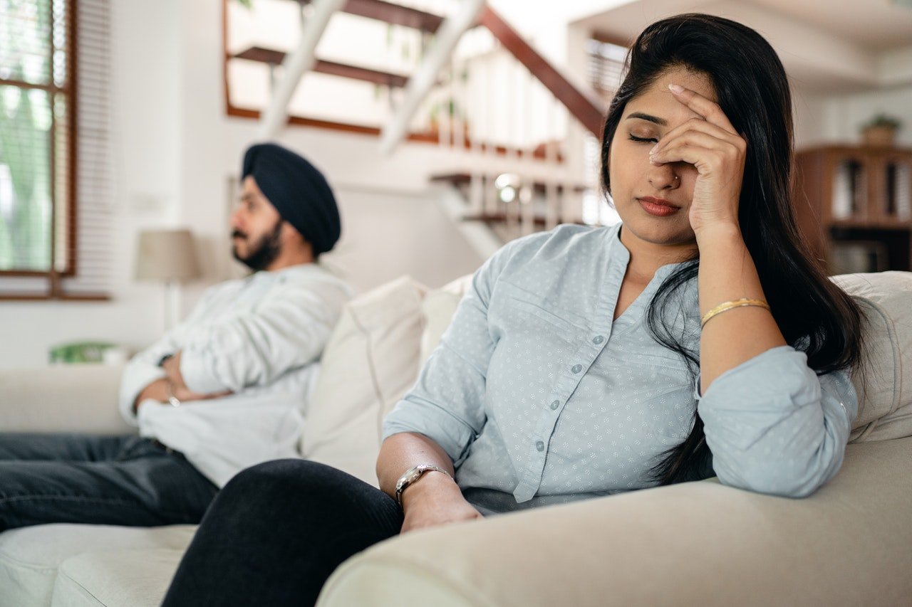 Man and woman sits on couch with woman holding her head in exasperation | Photo: Pexels