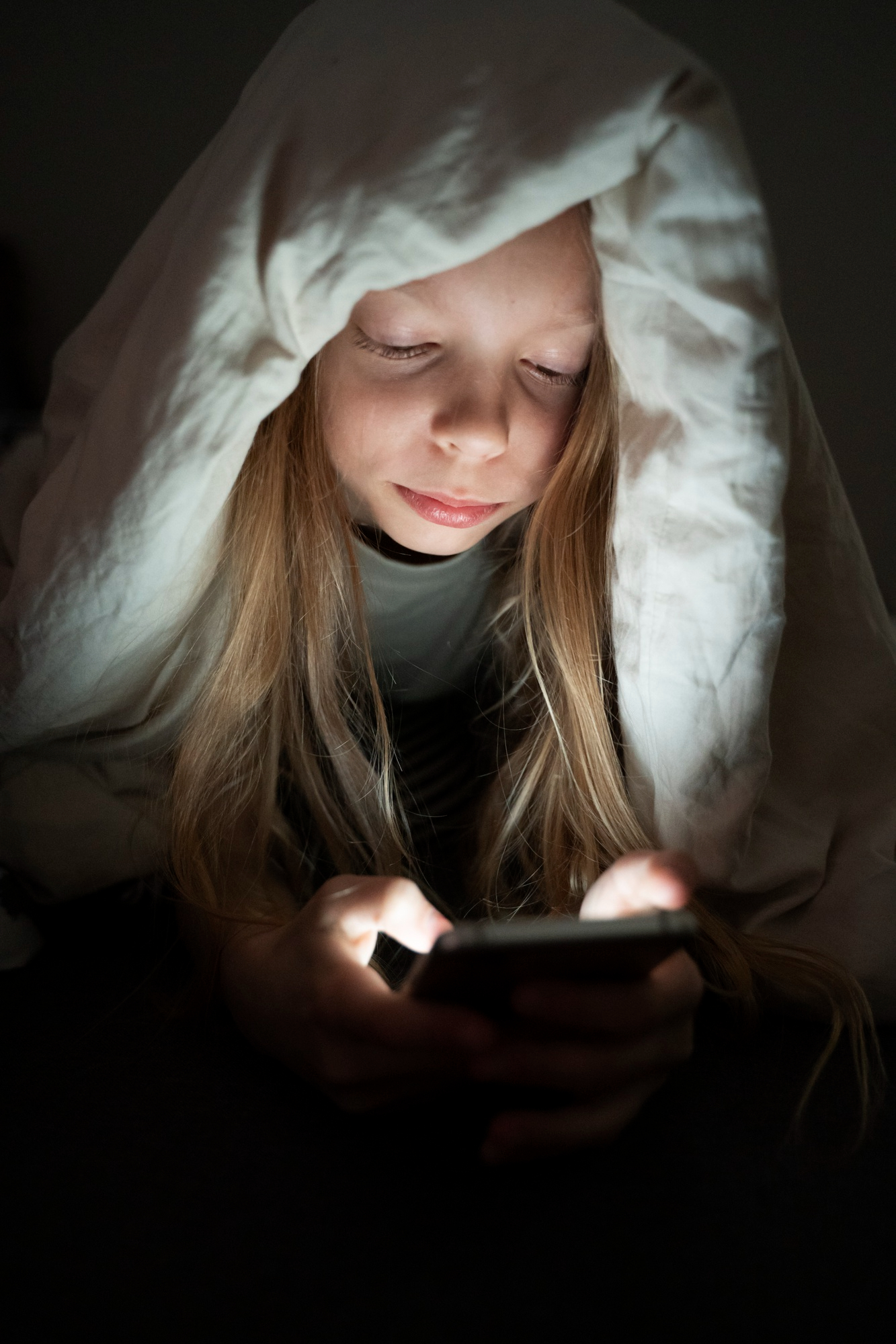 A little girl covered in a blanket while using her phone | Source: Freepik