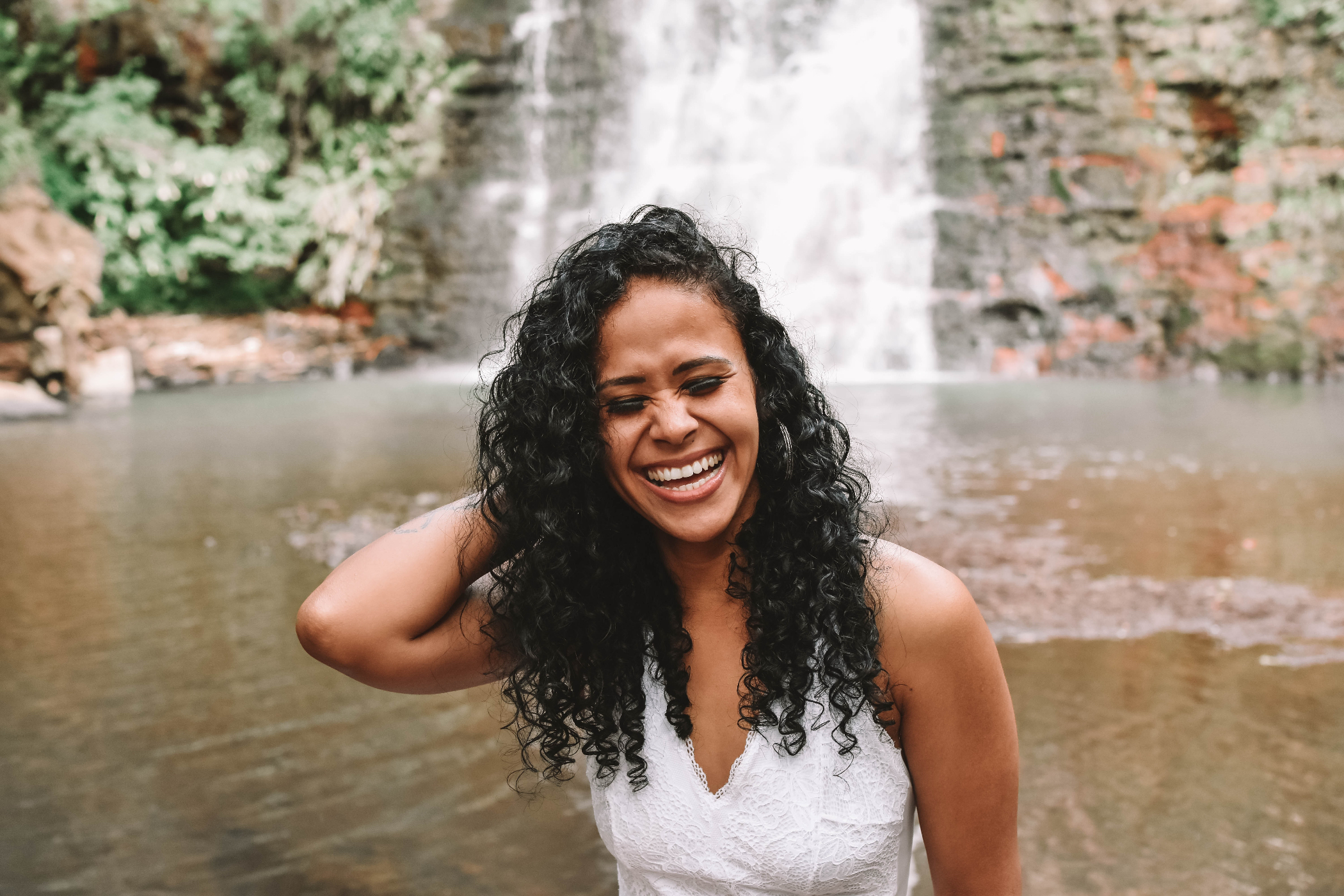 Woman laughing in front of a waterfall. | Source: Pexels