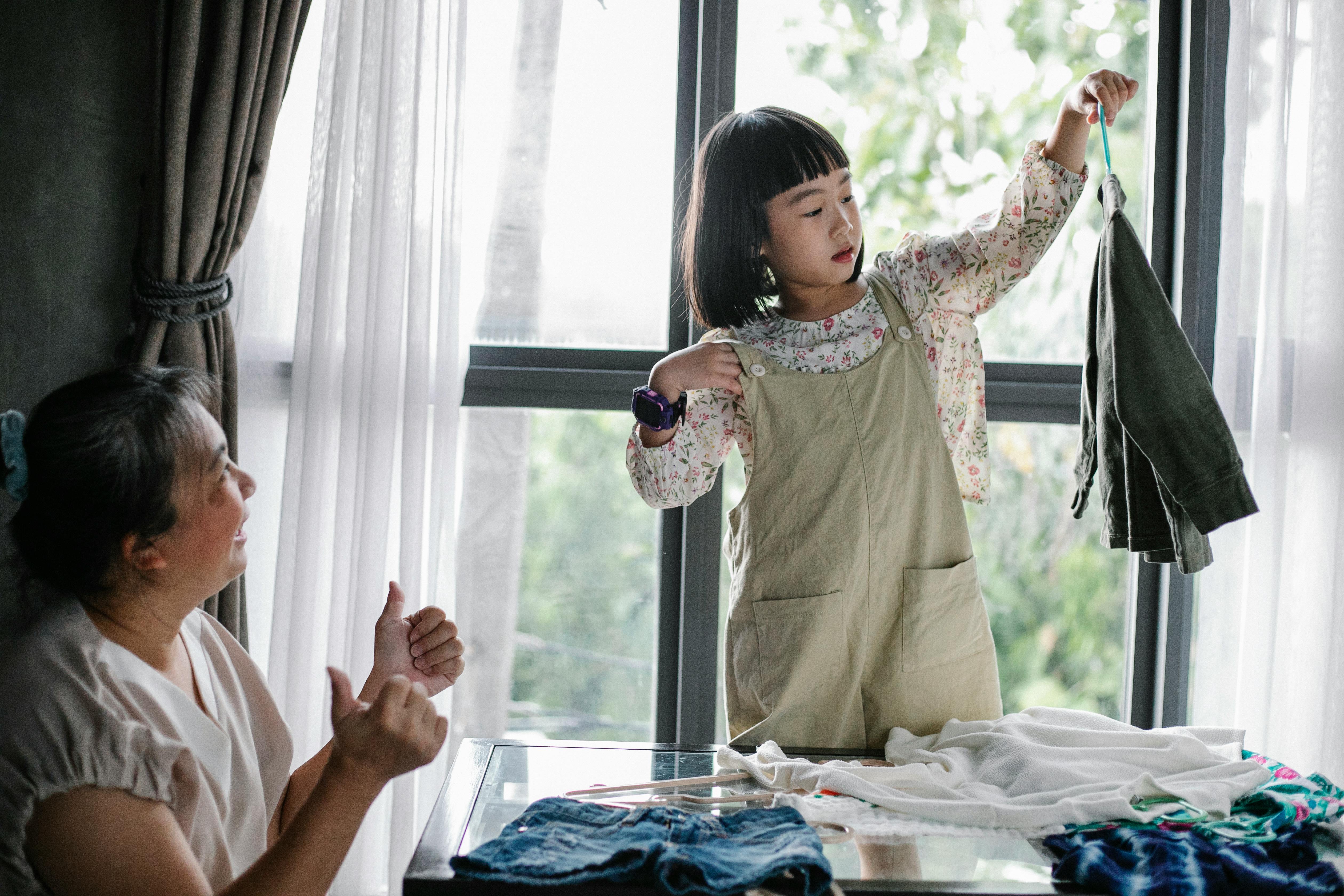 A little girl's mother proud of her for being able to hang up her own clothes | Source: Pexels