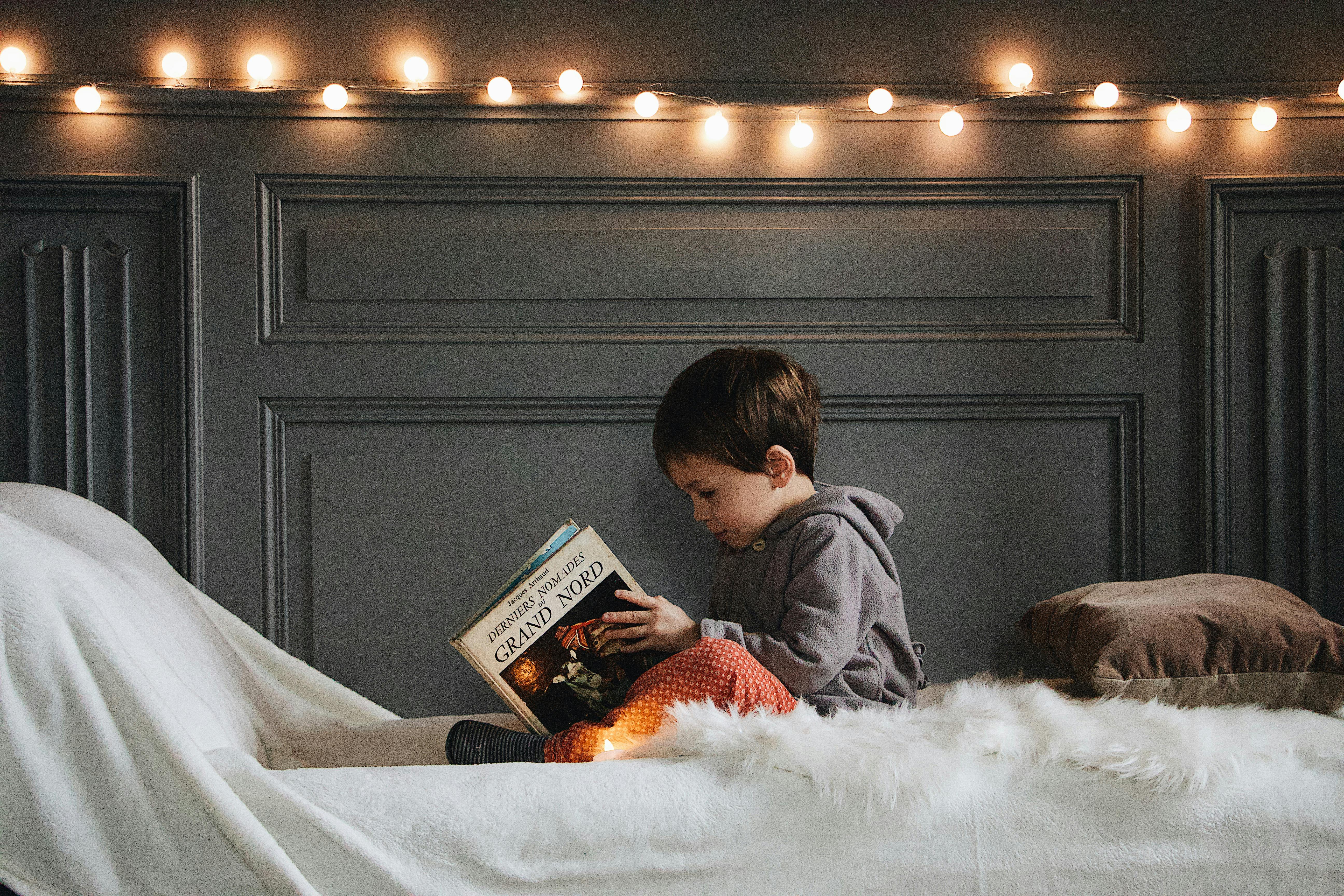 A small boy reading a book in bed | Source: Pexels