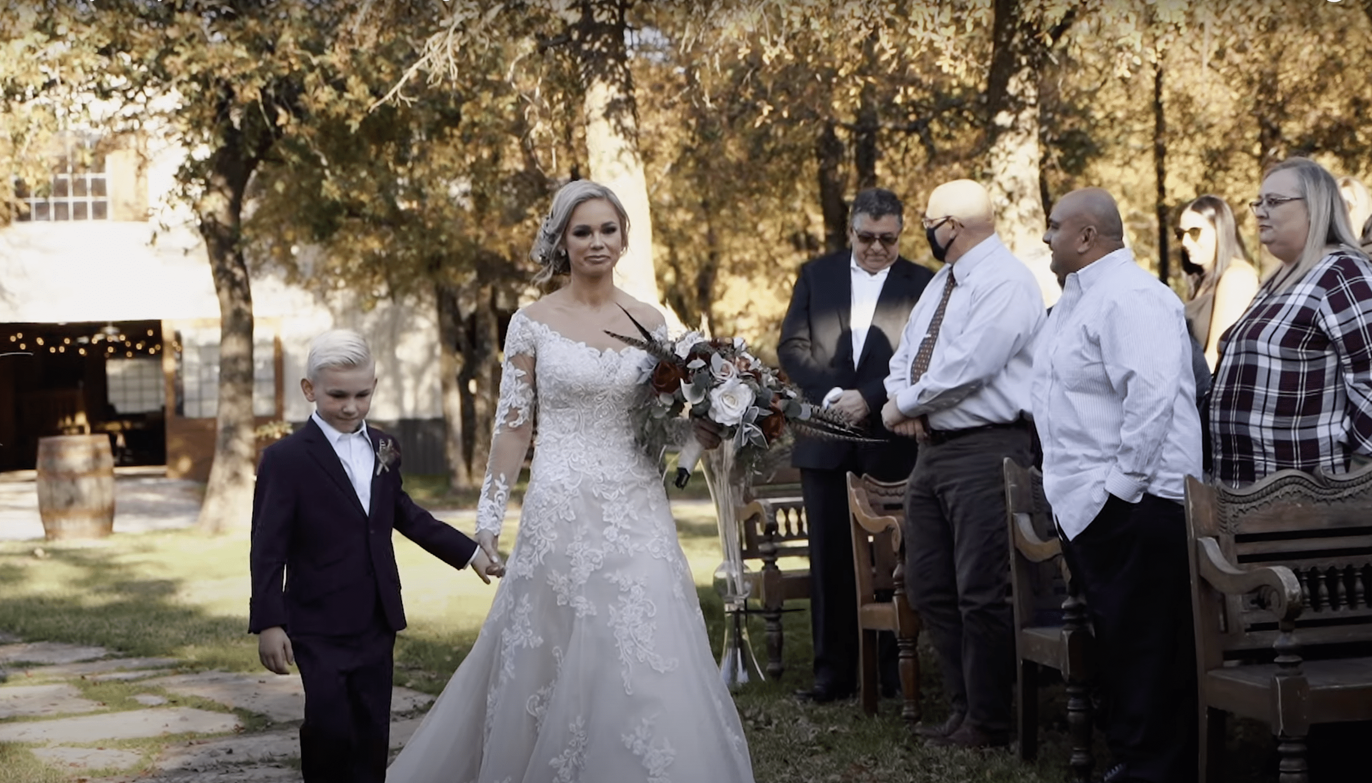 Whitney walking down the aisle while holding hands with her son, Jaden. | Source: Youtube.com/BSR Wedding Films