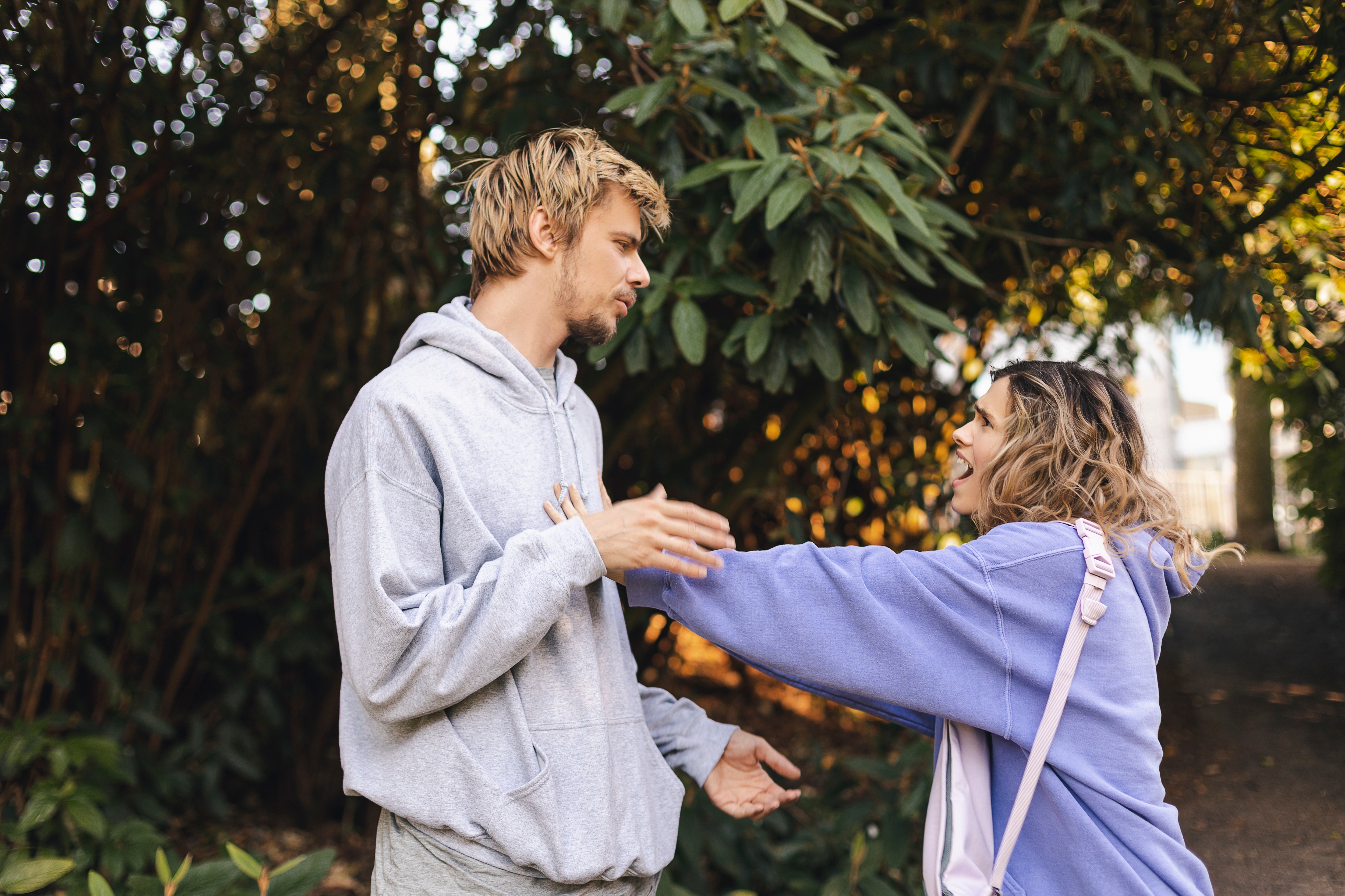 Upset woman in a hoody pushes the man to the side in the park | Source: Shutterstock.com