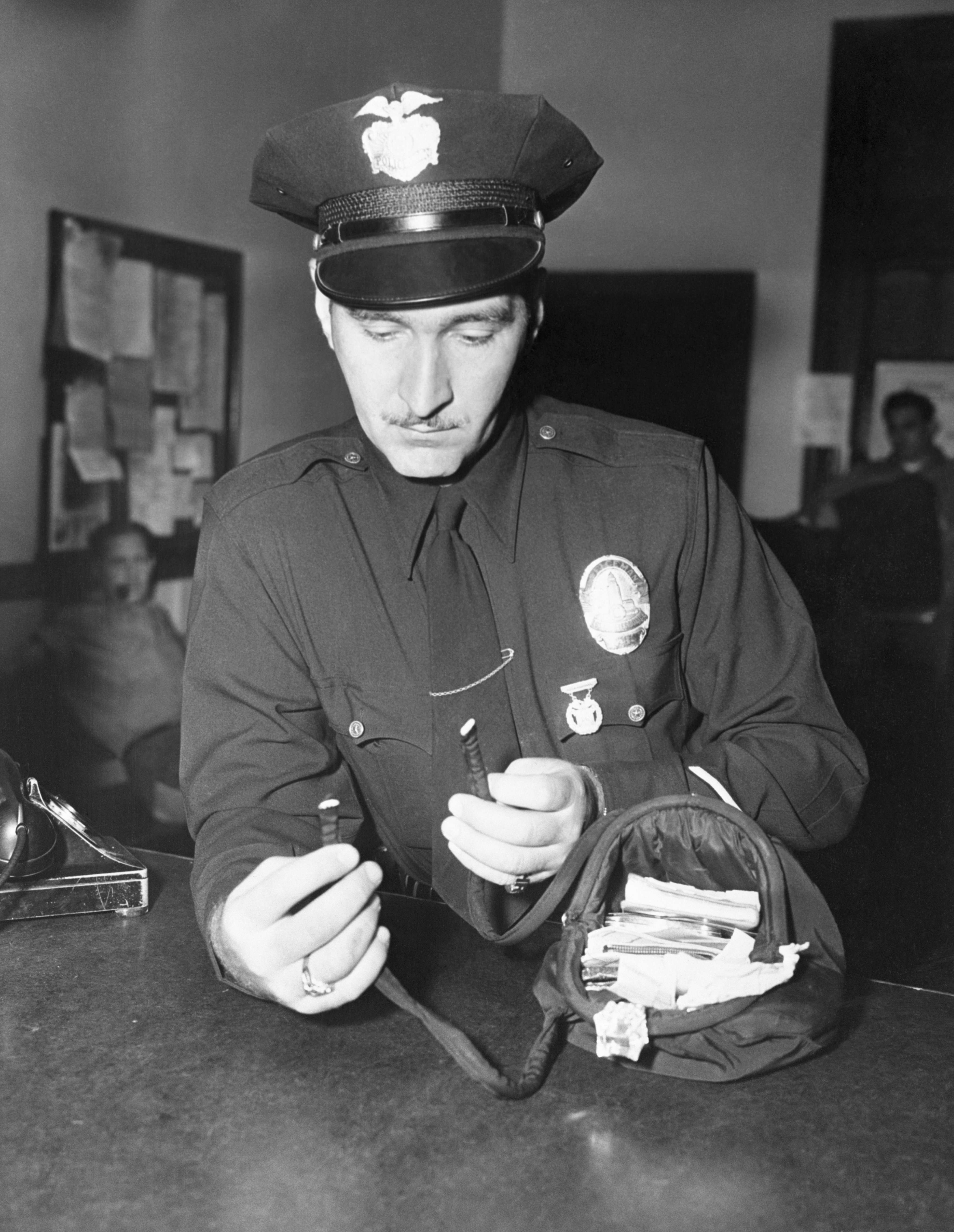 L'agent Howard Rose tenant le sac à main endommagé de Jean Spangler, qui a été recueilli comme preuve, 1949 | Photo : Getty Images