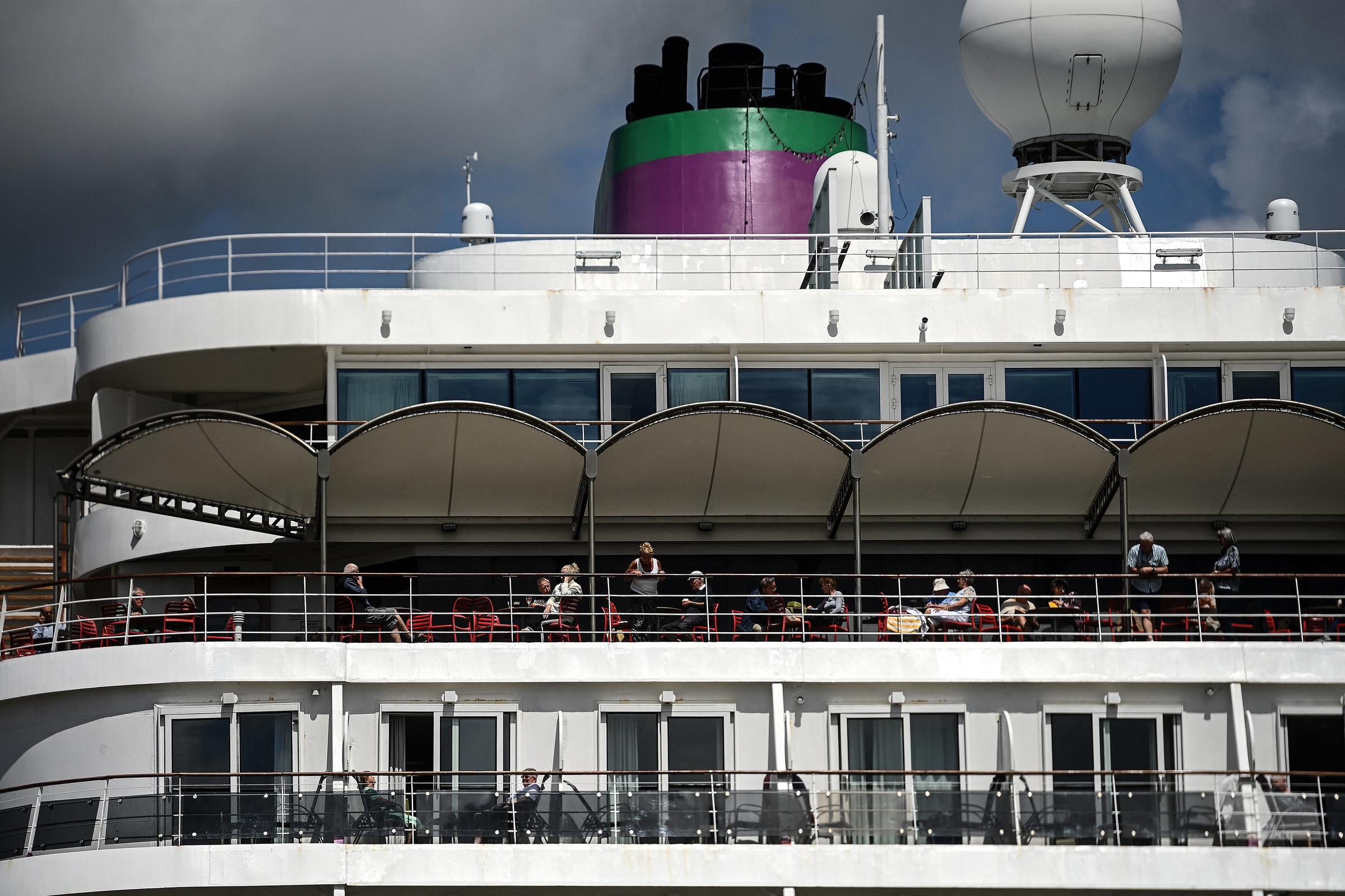 Passengers stand aboard the Bahamas-registered cruise ship Ambition after they were confined following the outbreak of a gastrointestinal illness onboard, at the Bordeaux port in Bordeaux, southwestern France on May 13, 2026. | Source: Getty Images