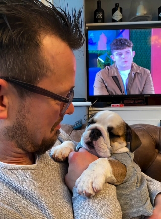 Adam Rickitt cradling a young Daphne while watching TV at home — from a post dated December 8, 2025. | Source: Instagram/katyrickitt