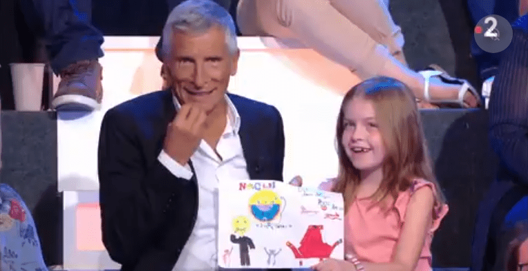 Nagui et une petite fille qui montre le dessin. | Photo : GettyImage