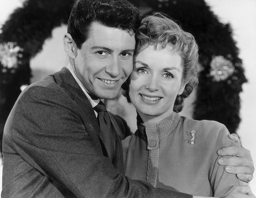 American singer Eddie Fisher smiling and embracing his wife, Debbie Reynolds, in front of a holiday wreath circa 1957. | Photo: Getty Images