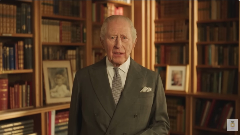 Standing in a wider shot of the warmly lit room, King Charles III appears poised and dignified as he addresses the nation, the surrounding shelves and personal mementoes subtly reinforcing the intimate and reflective tone of his message marking his late mother's milestone birthday. | Source: YouTube/The Royal Family Channel