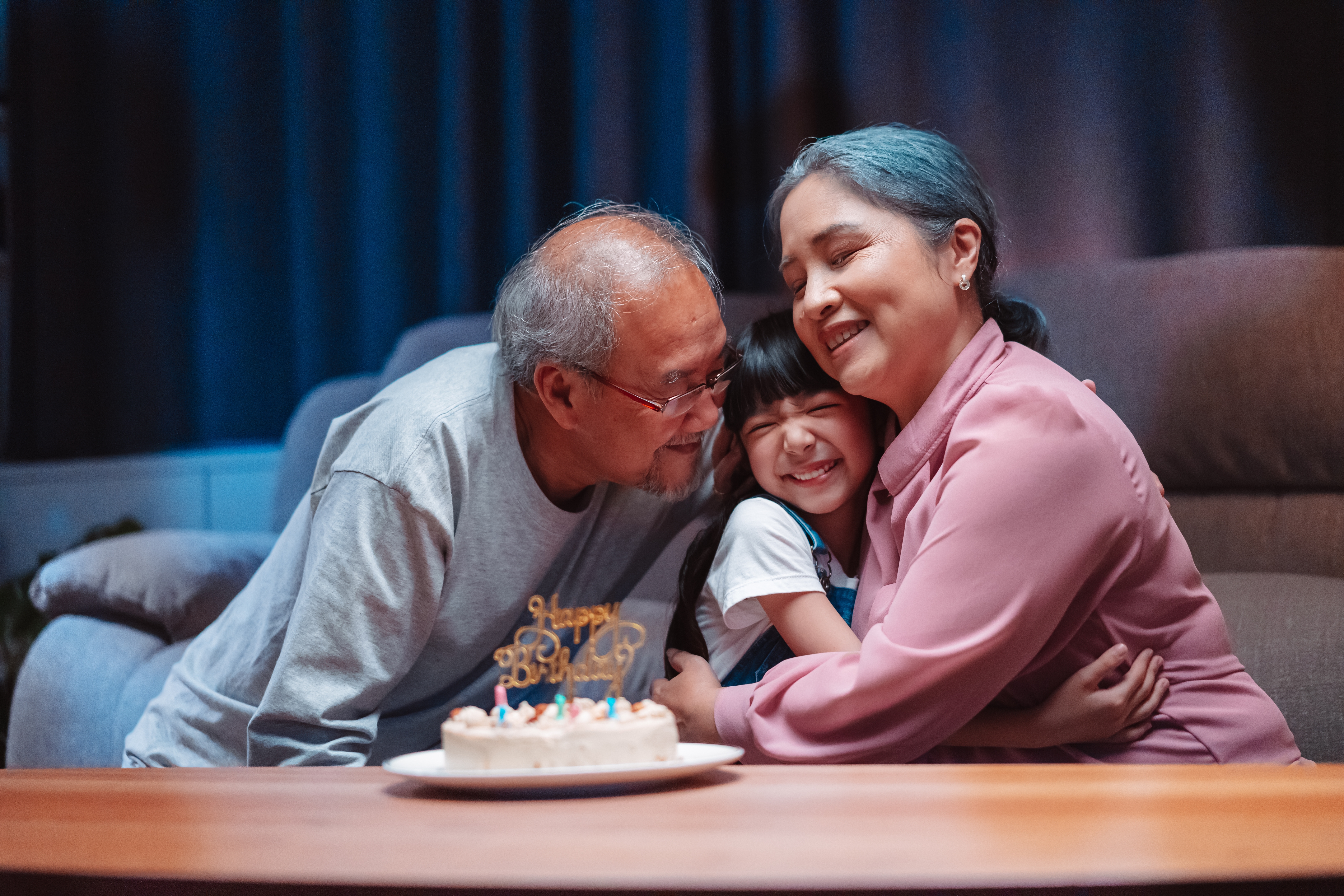 Grandparents hug their granddaughter as they sit in front of a birthday cake | Source: Shutterstock