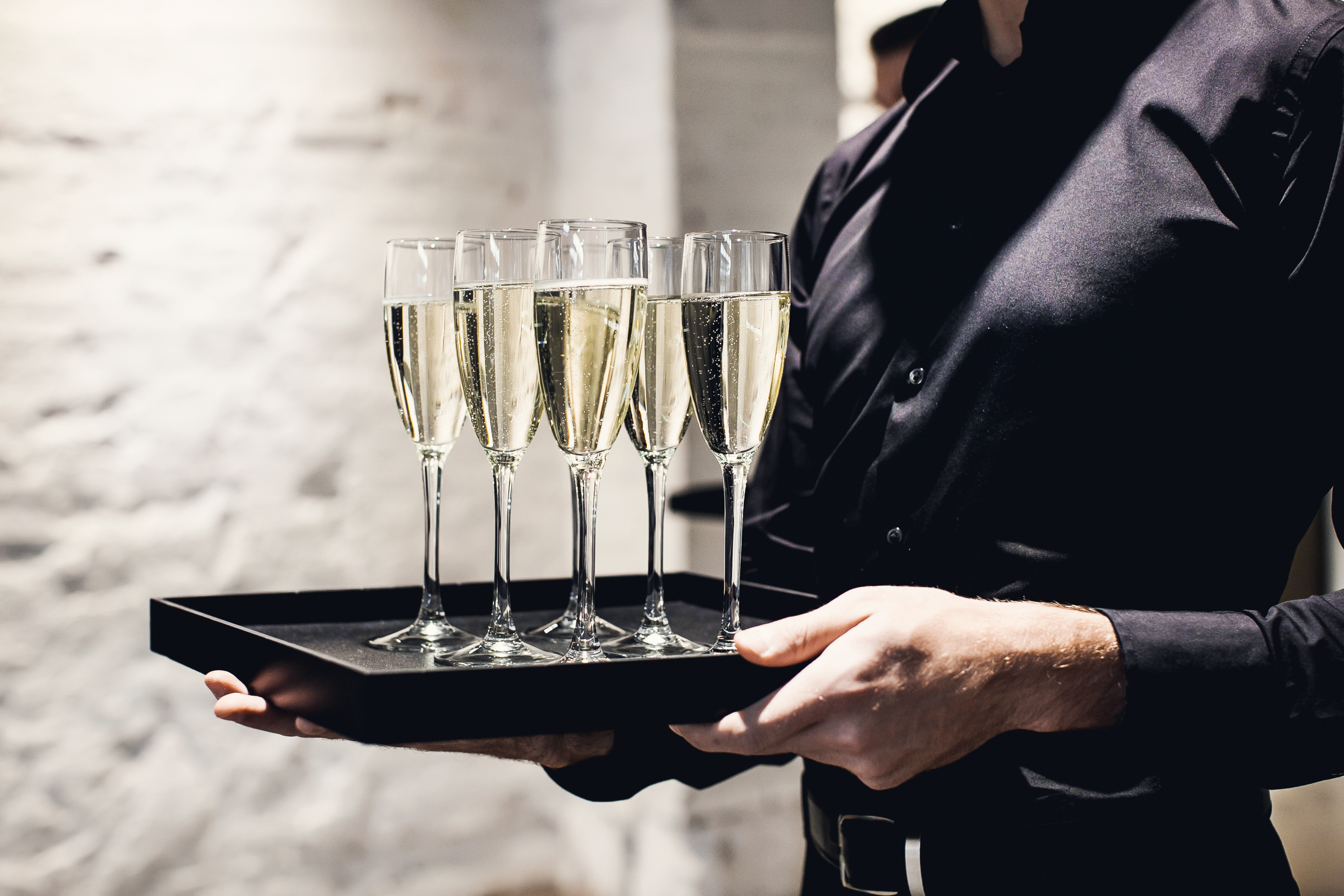 A waiter holding glasses with champagne served on a tray. | Source: Shutterstock