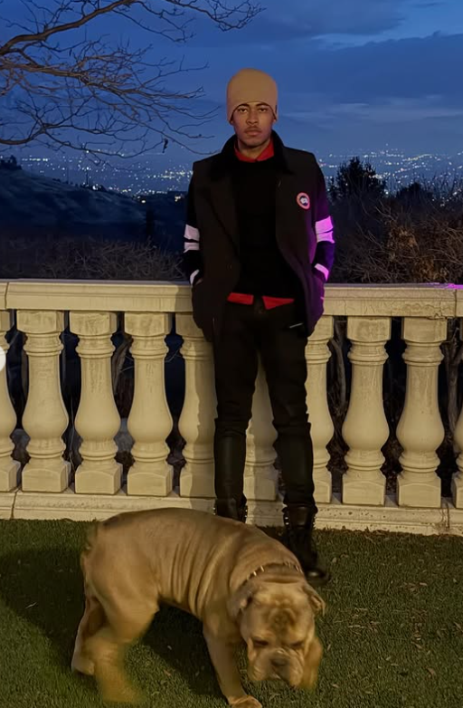 Robert Cosby Jr., stands with his hands in his pockets as his dog plays in front of him. | Source: Instagram/illboybubs