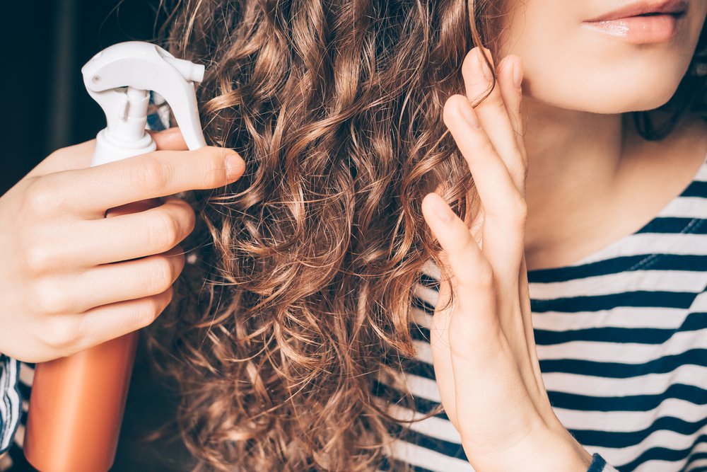Mujer aplicando spray en su cabello rizado. | Foto: Shutterstock
