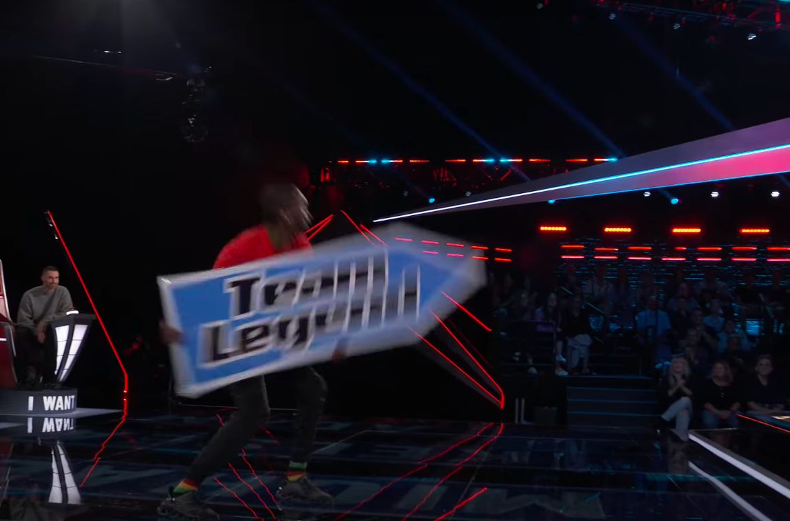 The sign spinner spinning a Team Legend sign. | Source: YouTube/The Voice