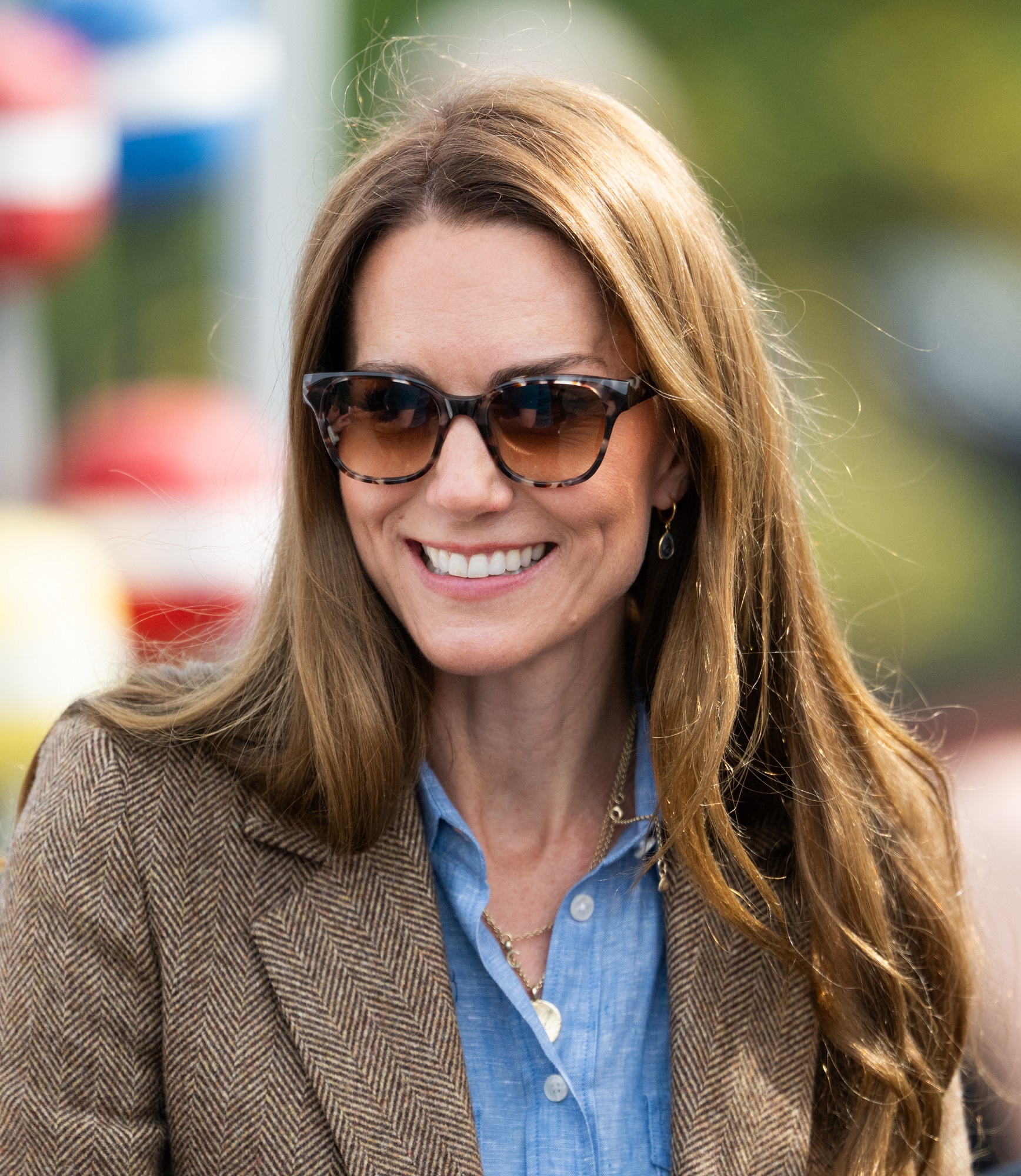 Catherine smiles brightly in the sunlight while visiting a local market in Tobermory, her face framed by softly tousled golden-brown hair that glows in the light. With dark sunglasses and a relaxed expression, she radiates warmth and ease during the outing.