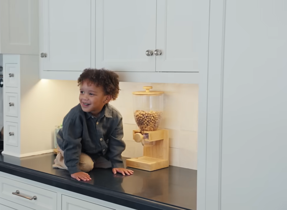 Caught in the act! Little Leo flashes a mischievous smile while hanging out next to his favorite cereal dispenser. | Source: YouTube/@Archdigest